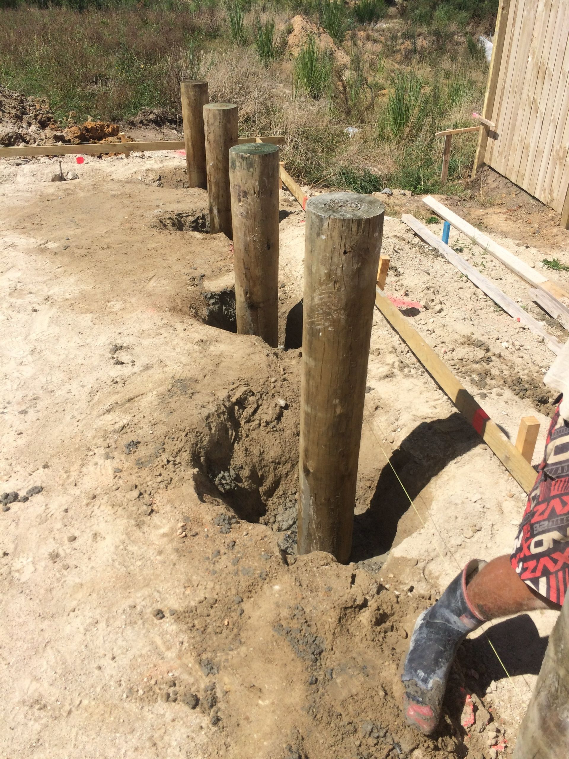 Wooden fence posts set in holes, awaiting concrete. Construction site.