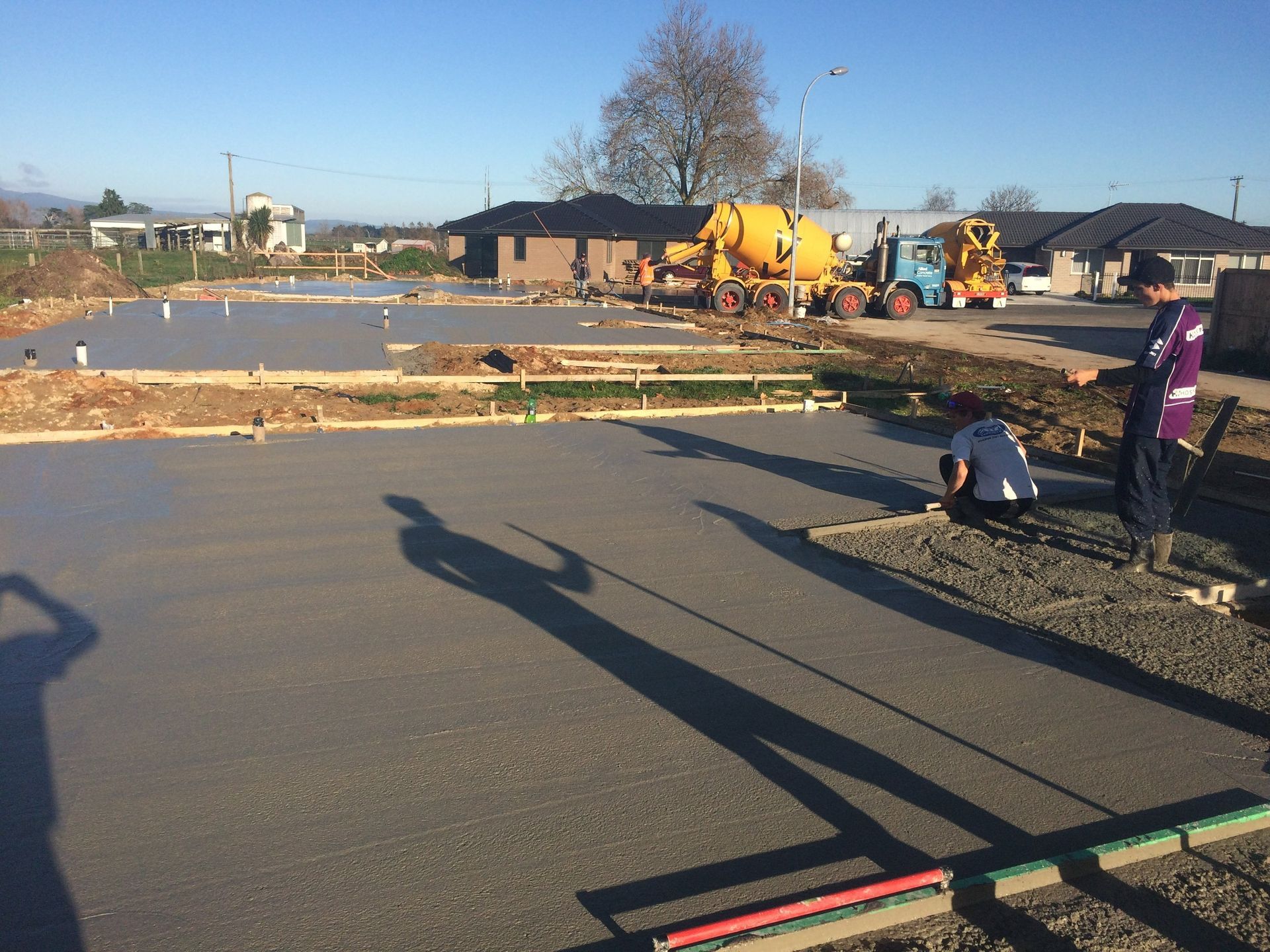 Workers pouring and smoothing fresh concrete foundation at a construction site on a sunny day.
