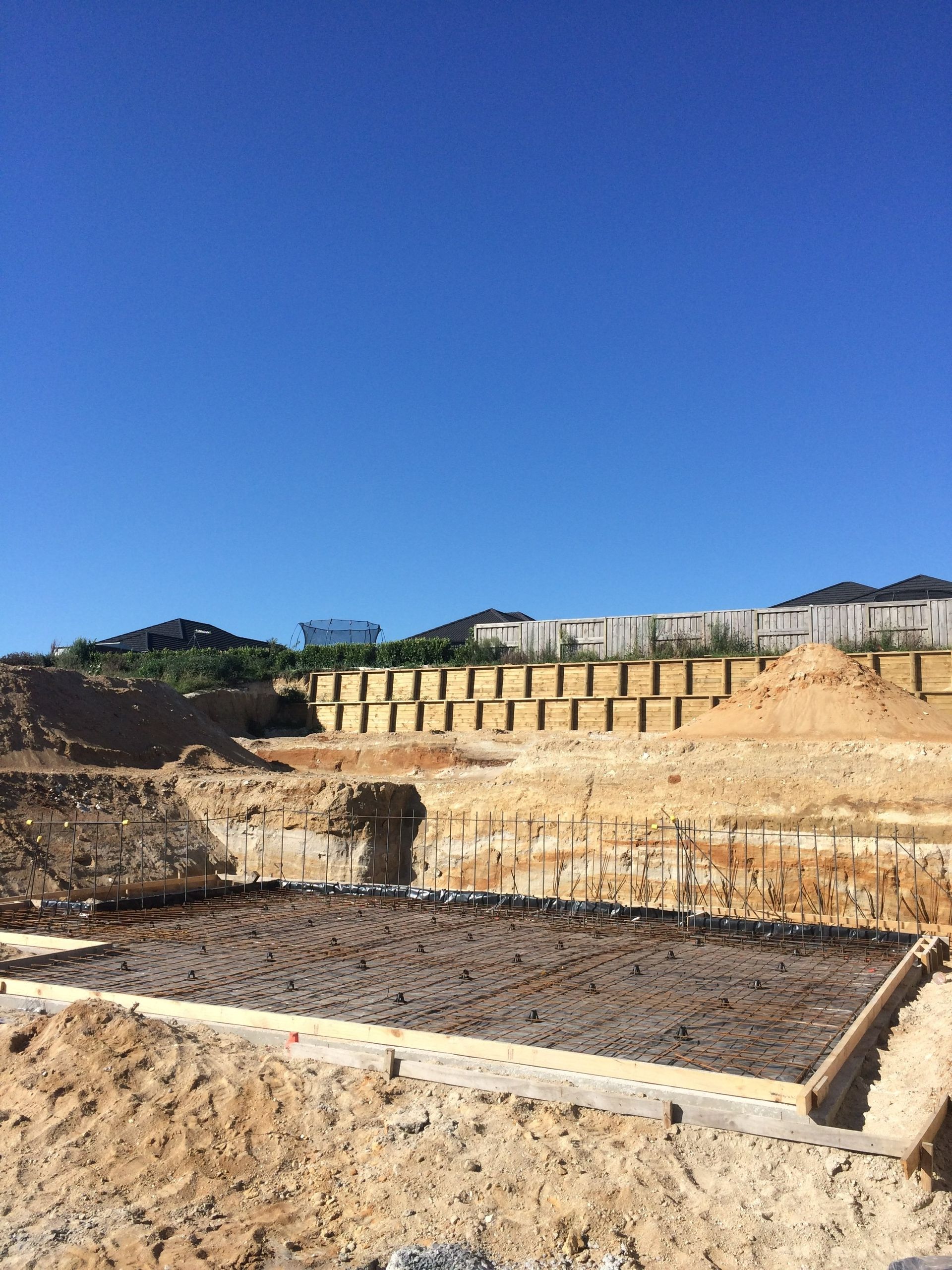 Construction site with tiered retaining walls under a bright blue sky.