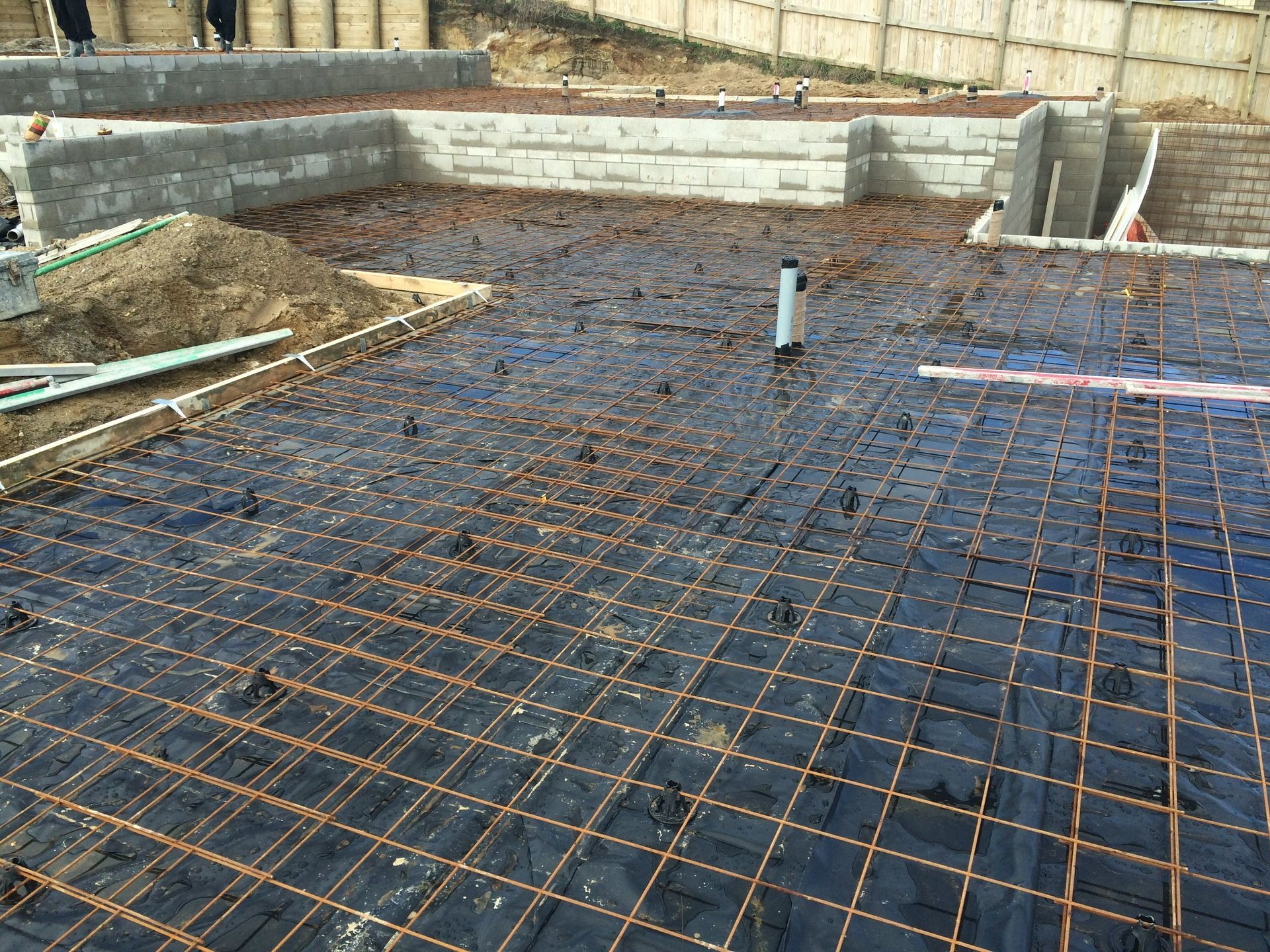 Construction site: Rebar grid laid over black sheeting, prepared for concrete pouring.