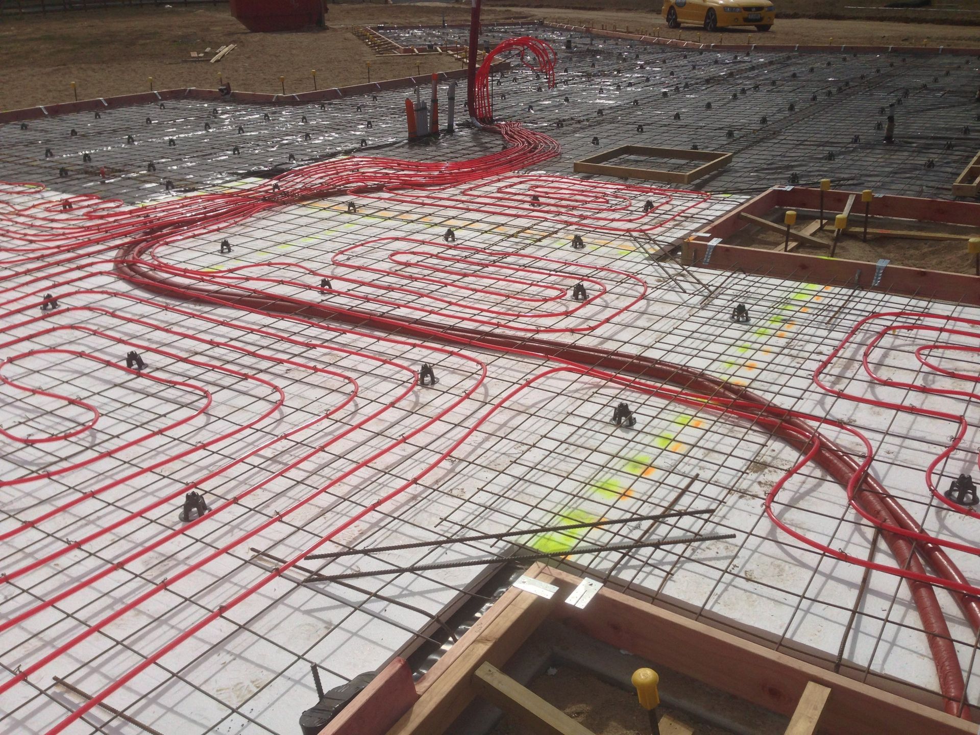 Red radiant floor heating pipes installed on a concrete slab, ready for pouring.