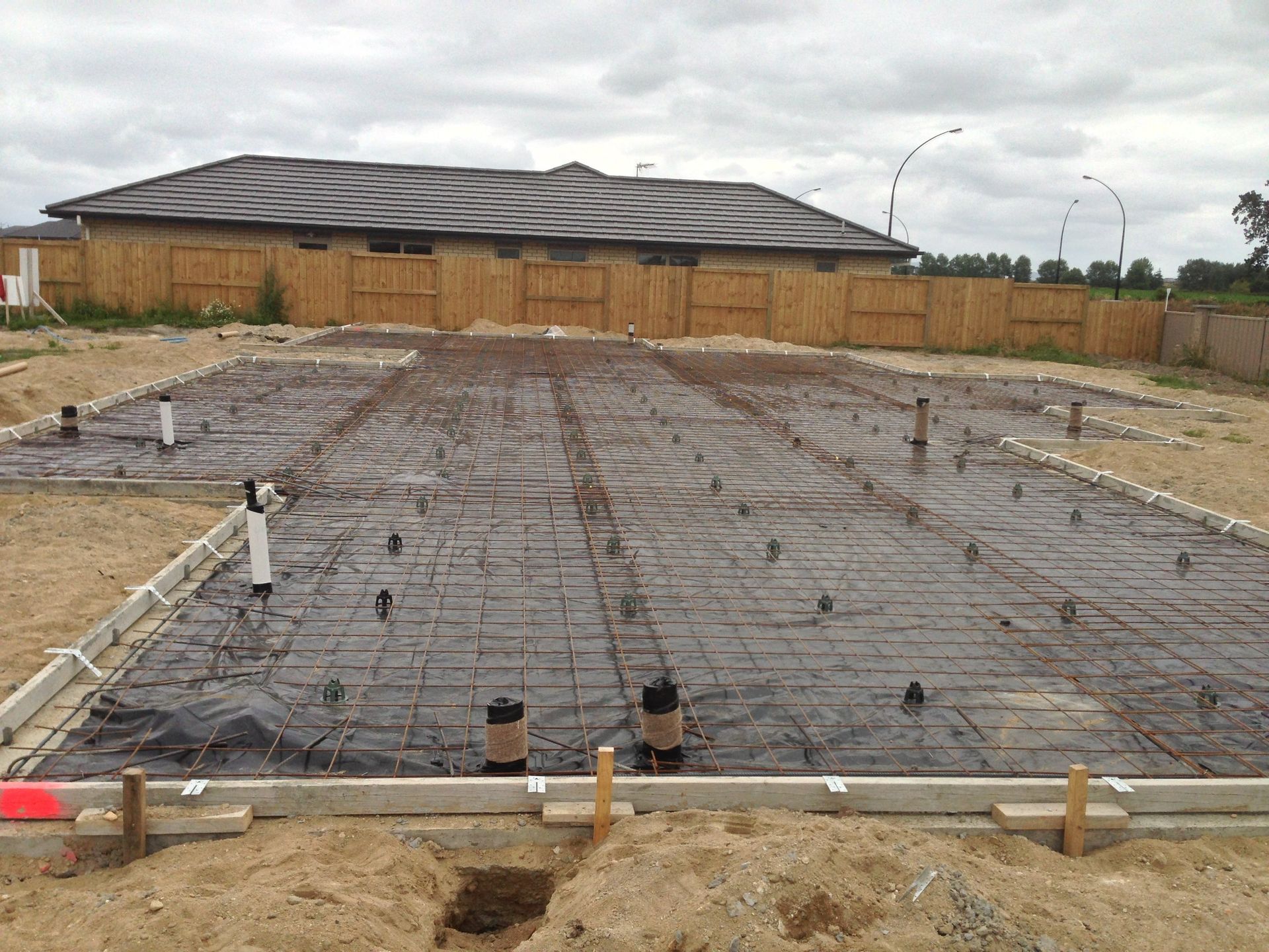 Foundation of a building under construction, rebar grid visible, with plumbing fixtures and concrete forms.