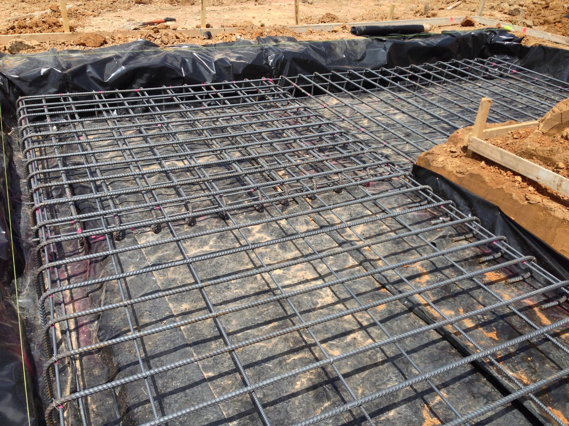 Reinforced steel rebar grid laid over a black liner in a construction site for a concrete foundation.
