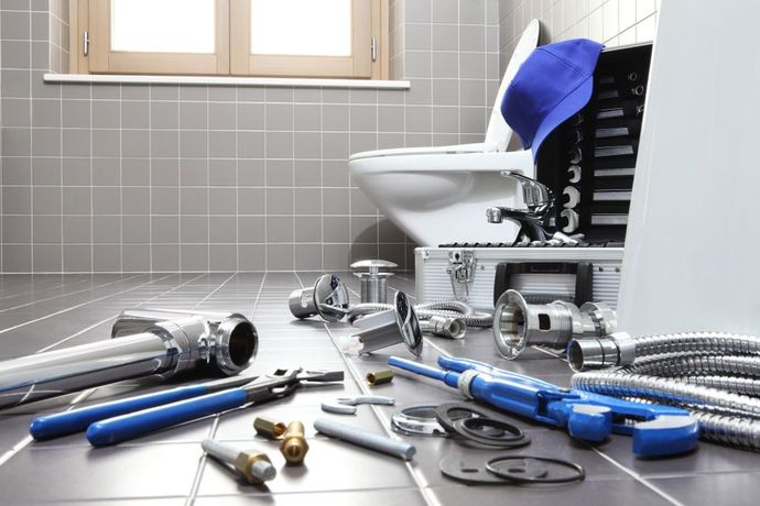 A bathroom with a toilet , sink , and plumbing tools on the floor.