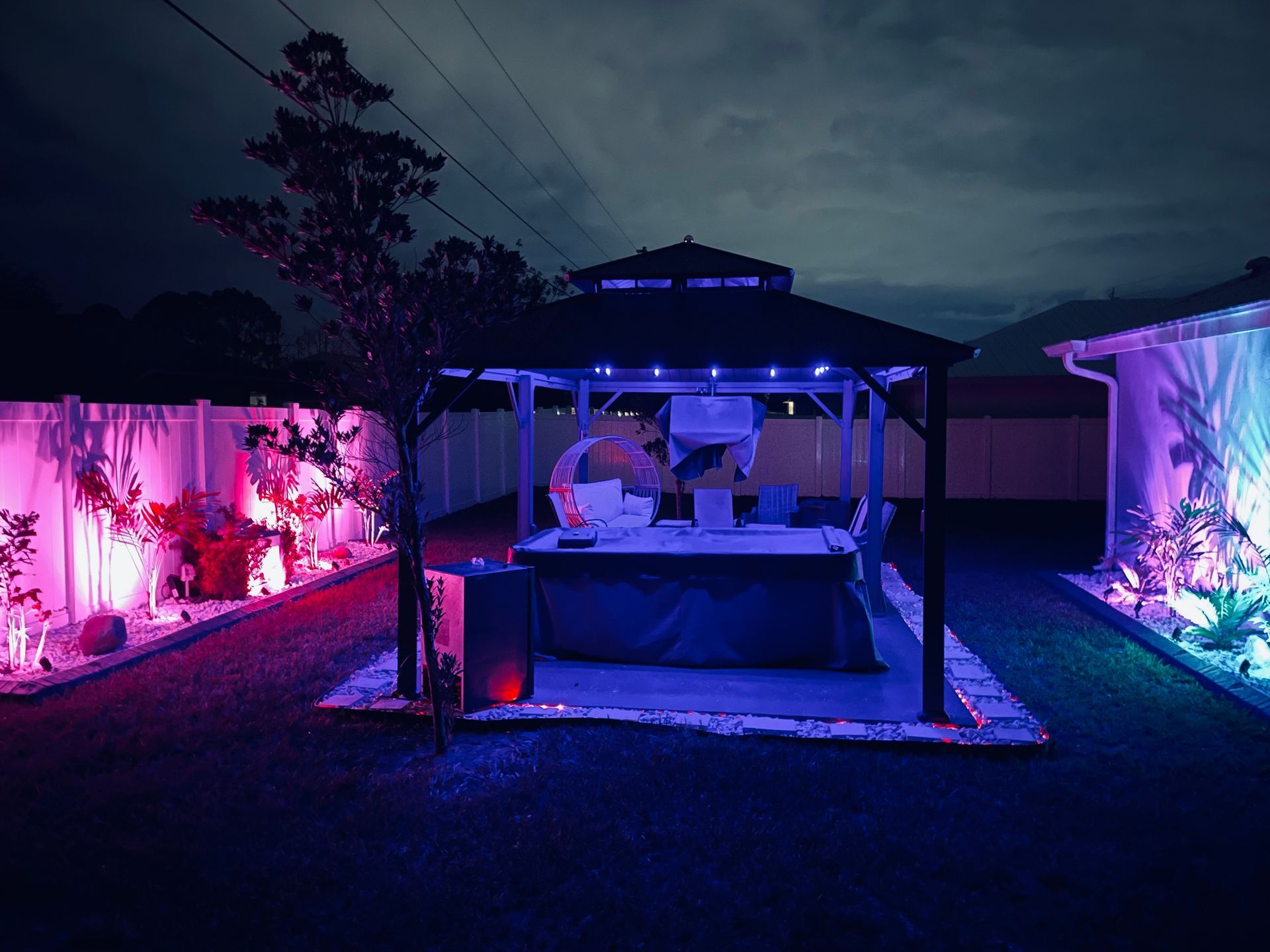 Backyard gazebo with colorful LED lighting at night.