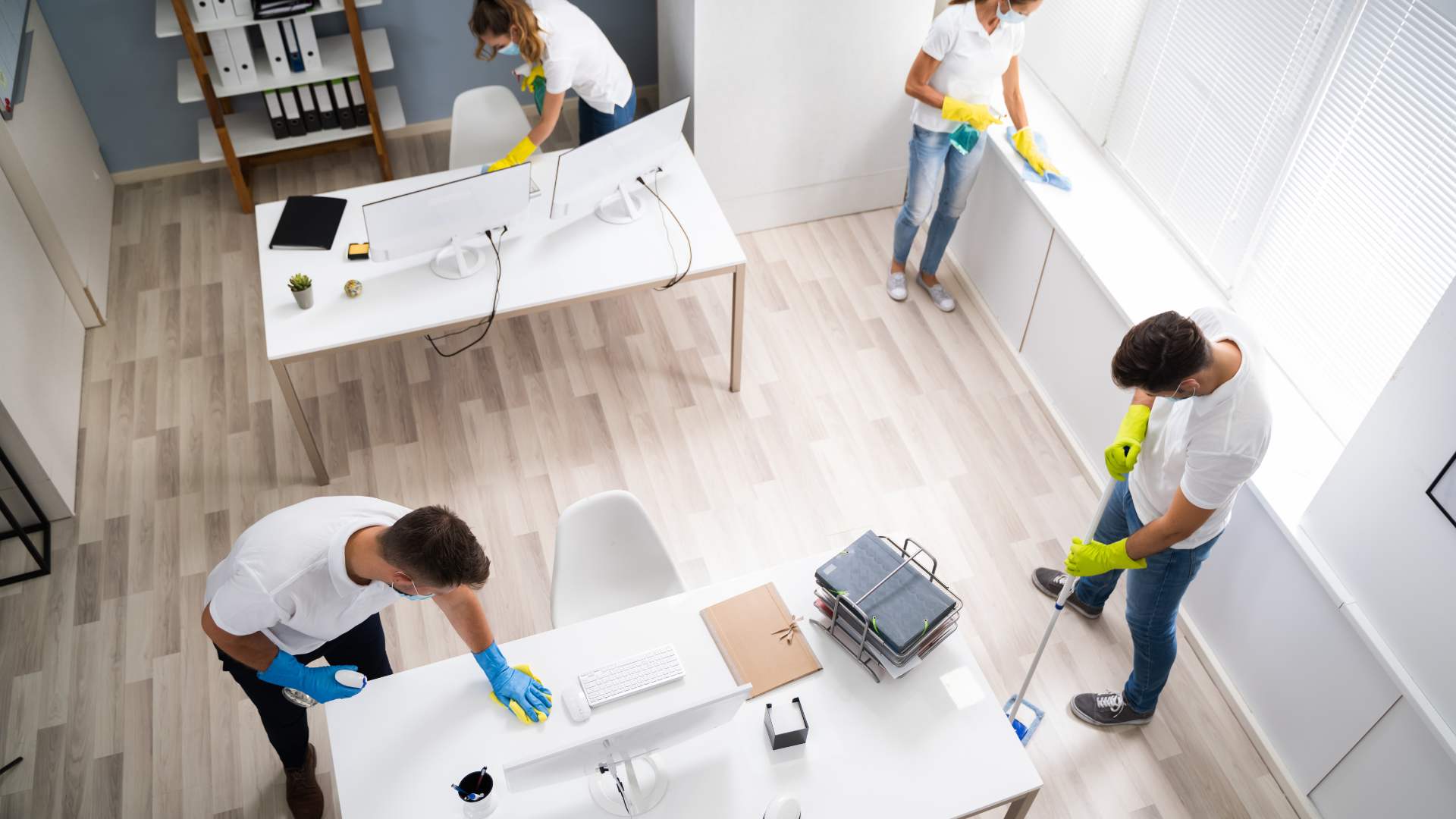 Office cleaners wiping surfaces: desks, window sill, with yellow gloves and white shirts.