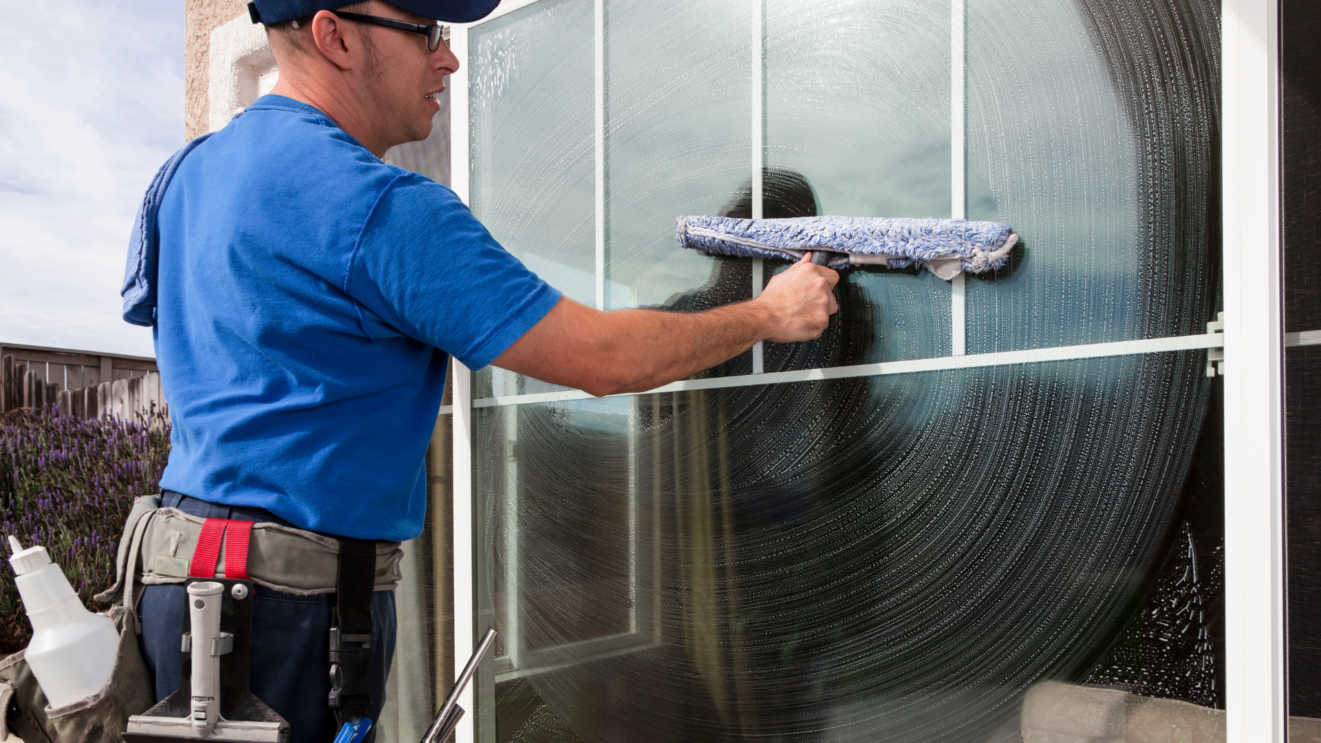 Man in blue shirt cleaning a window with a squeegee outside.