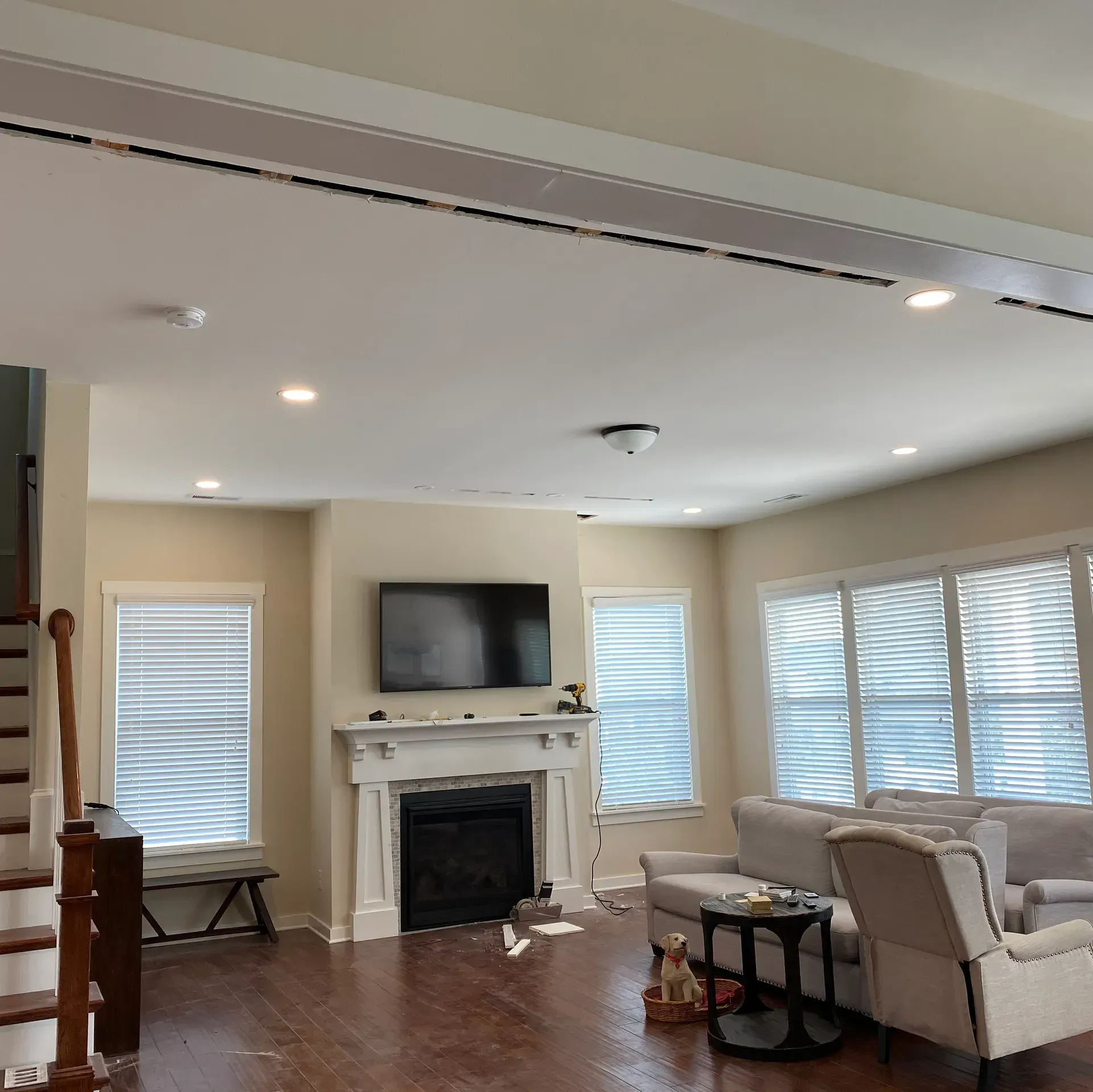 Living room with fireplace, TV, windows, and seating. Wooden floors, beige walls.