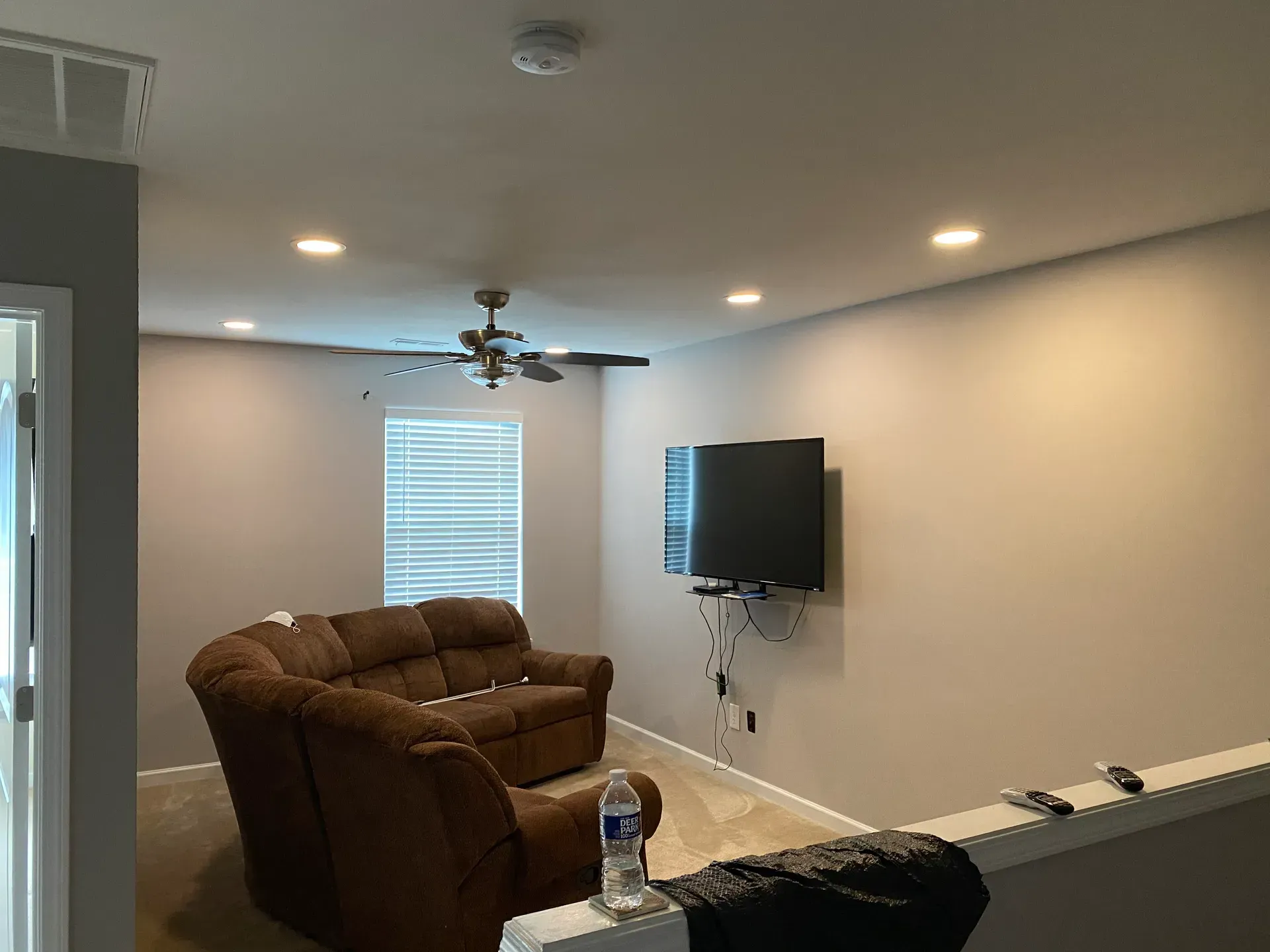 A living room with a brown recliner sofa, a TV on the wall, and ceiling lights.