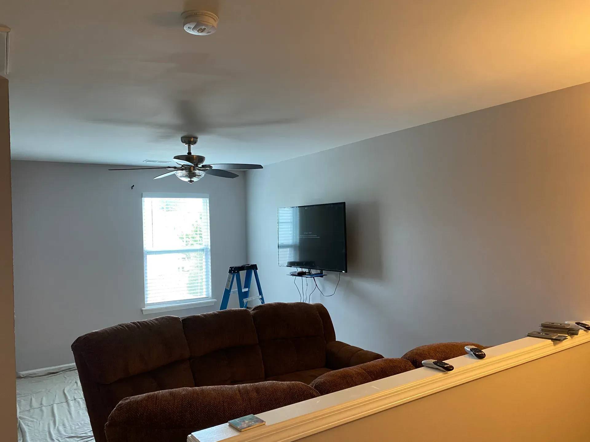 A living room with a brown recliner sofa, TV, window, and ceiling fan. Gray walls.