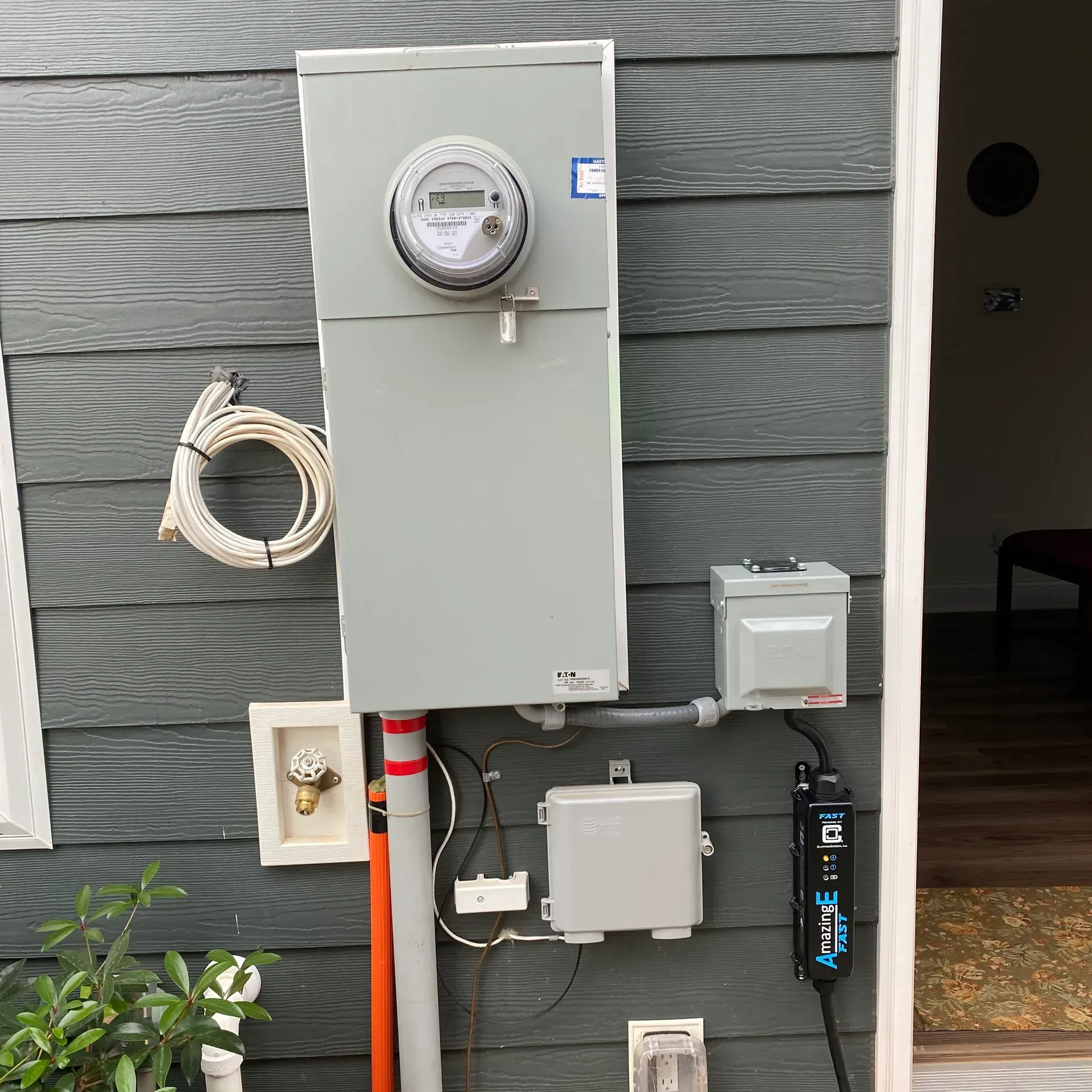 Electric meter box on a gray house exterior, with attached charging station for an electric vehicle.