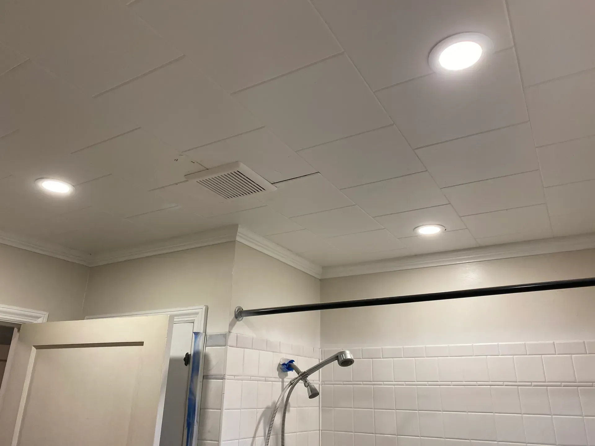 Bathroom ceiling with recessed lighting, shower head, shower curtain rod, and white tile.