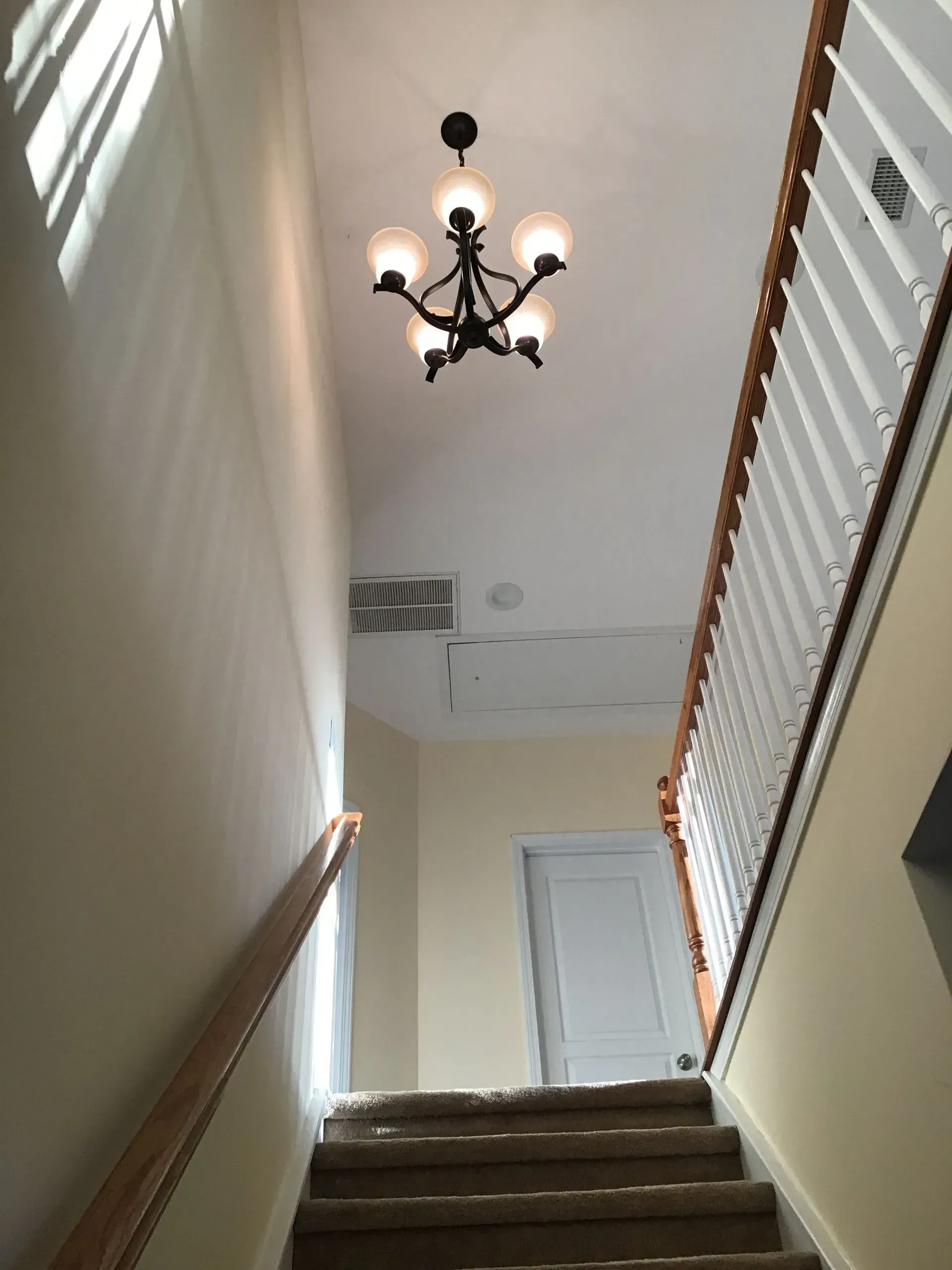 Staircase leading upwards with carpeted steps, white walls, and a chandelier hanging from the ceiling.