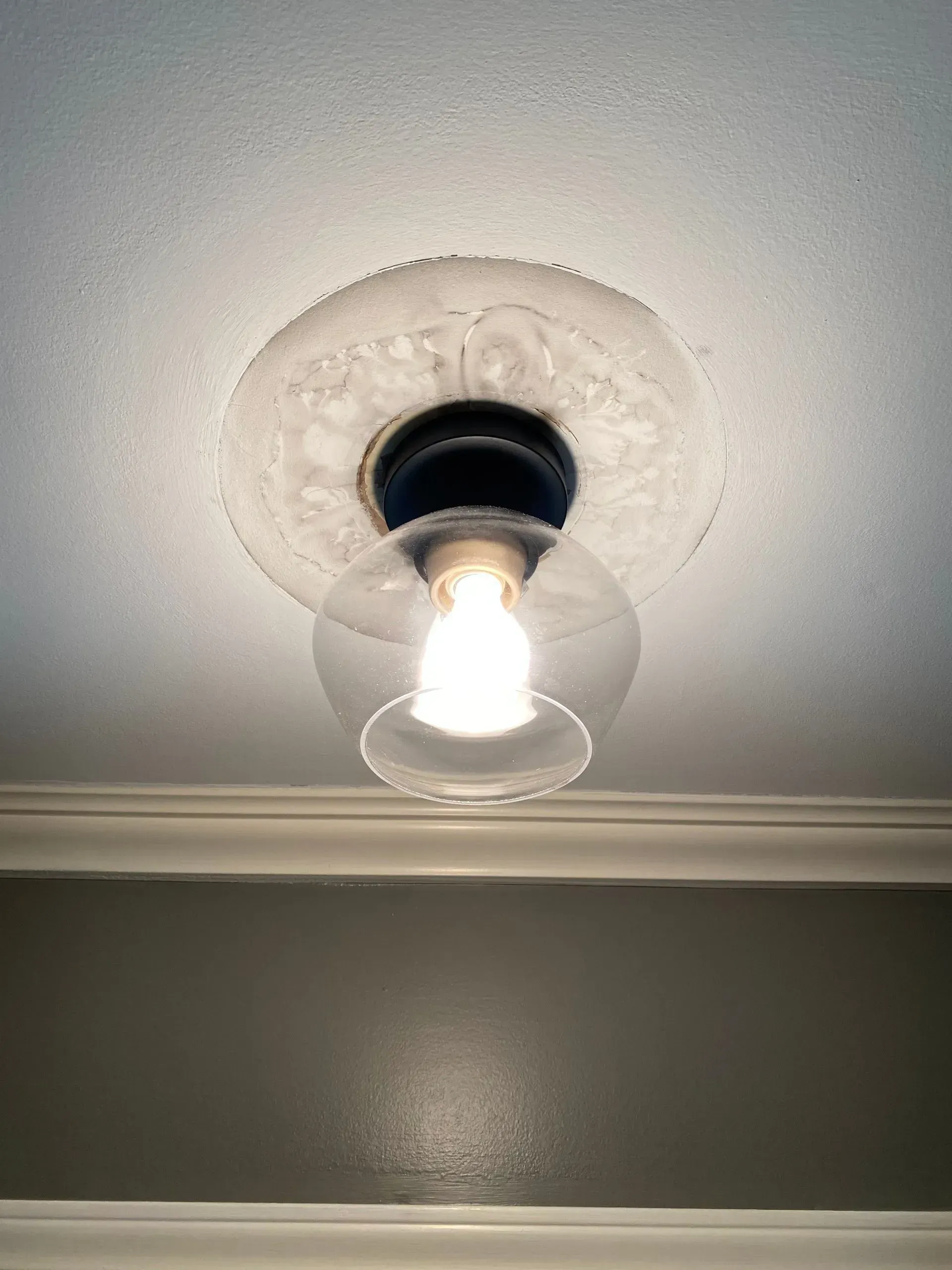 Ceiling light fixture with glass globe and black base. Mounted on white textured ceiling.