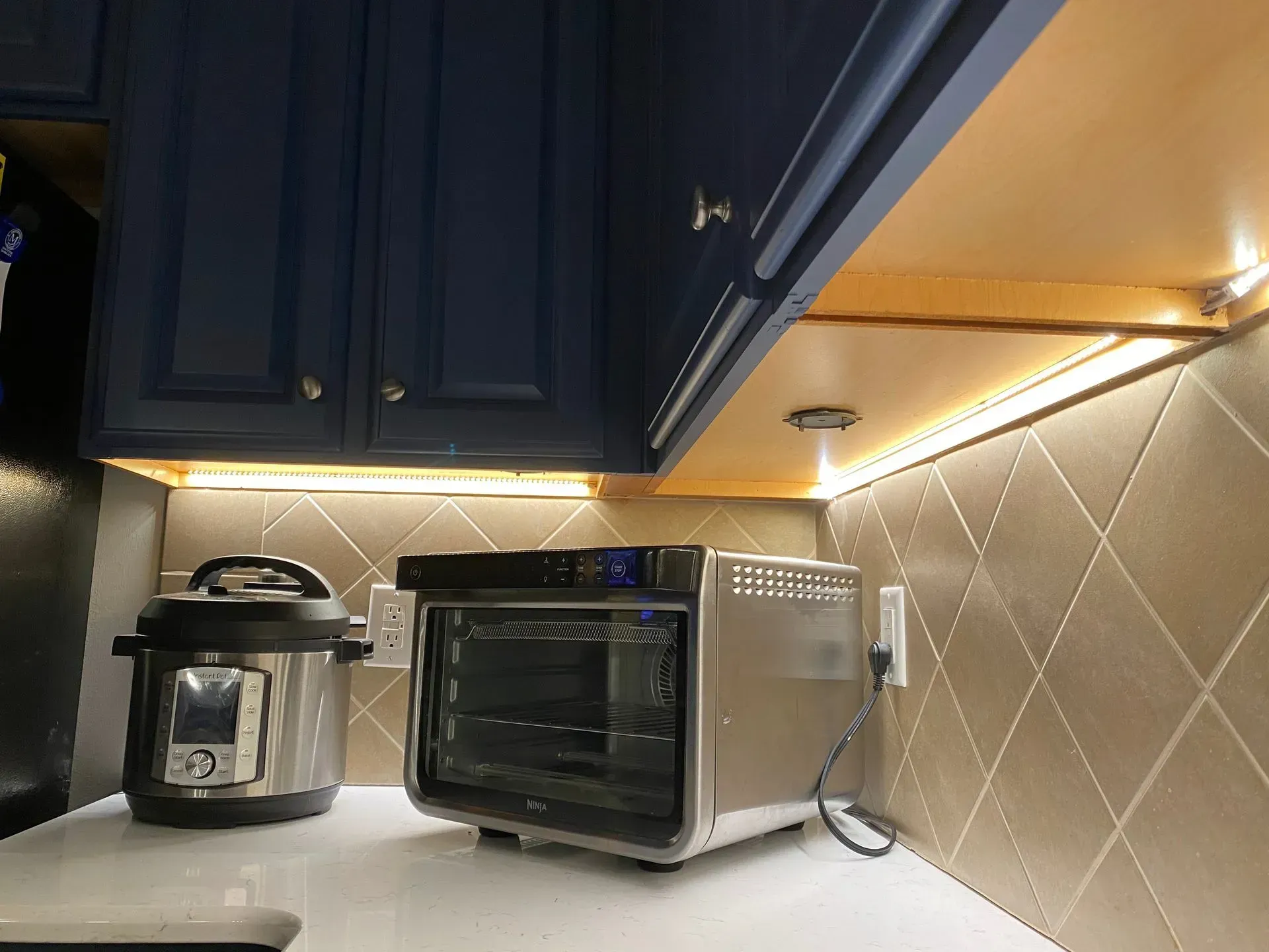 Kitchen with blue cabinets, under-cabinet lighting, and appliances including an Instant Pot and toaster oven.