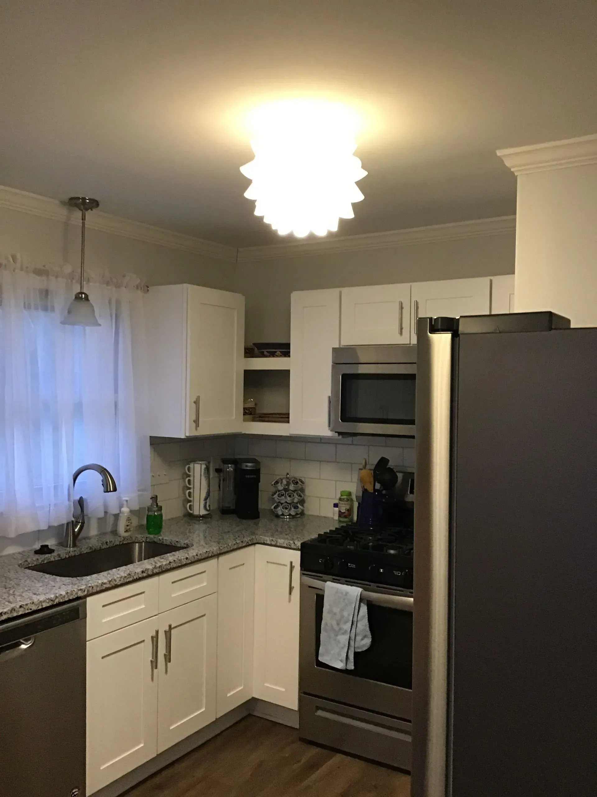Kitchen with white cabinets, stainless steel appliances, and a scalloped ceiling light.