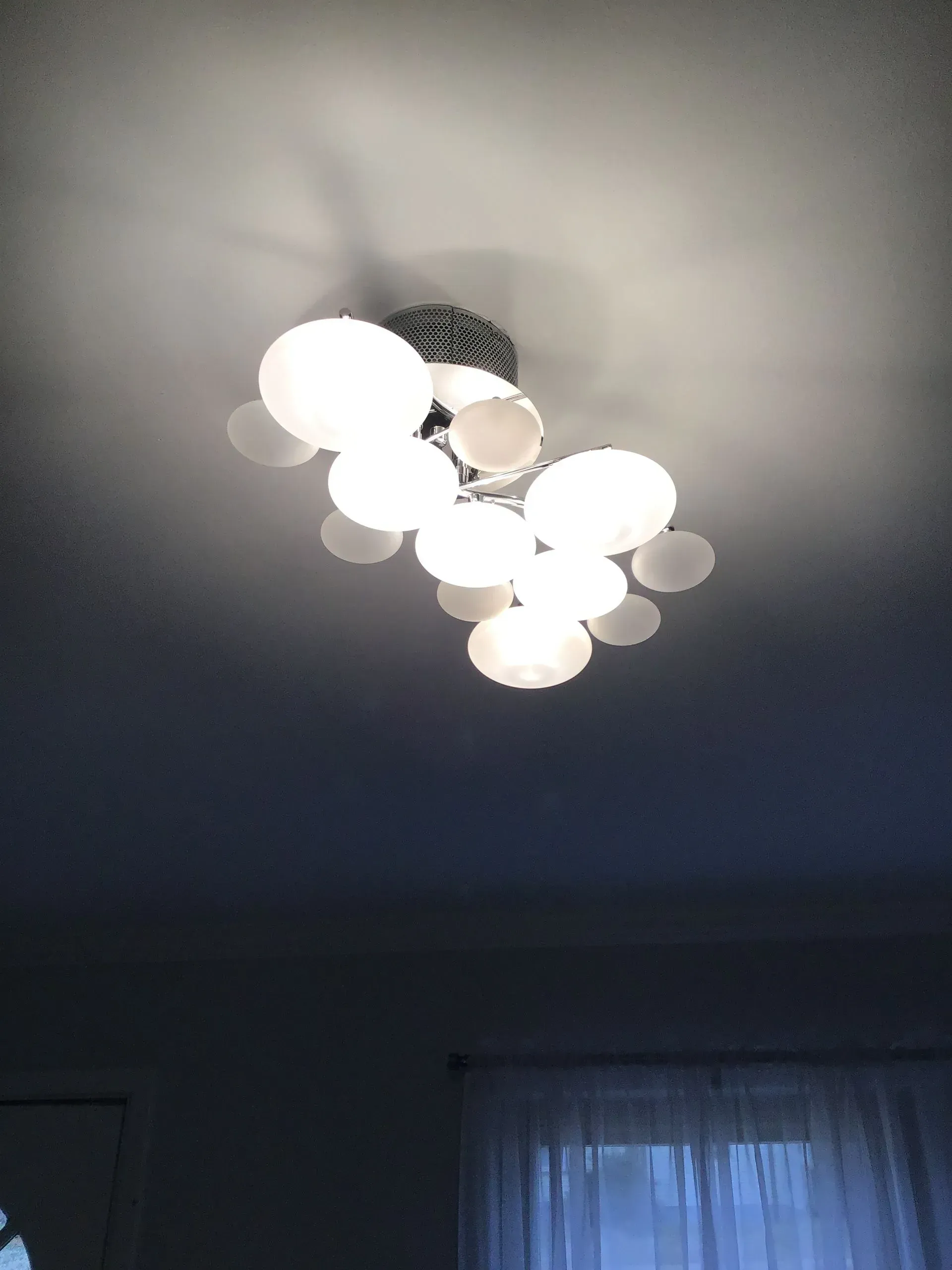 Ceiling light fixture with several round, frosted glass shades illuminating a room.