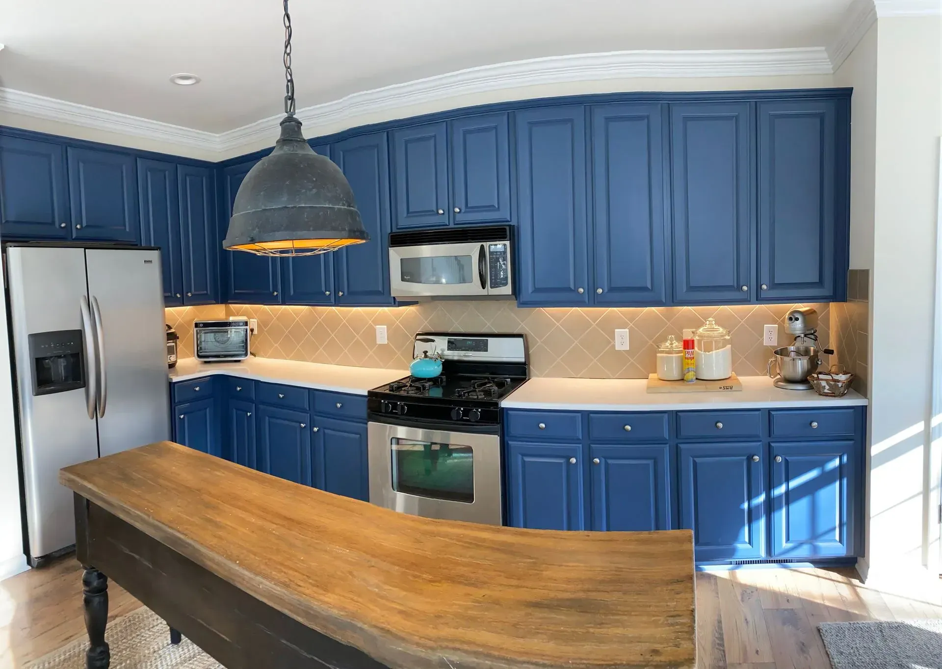 Blue kitchen with wooden island, stainless steel appliances, and cream backsplash.