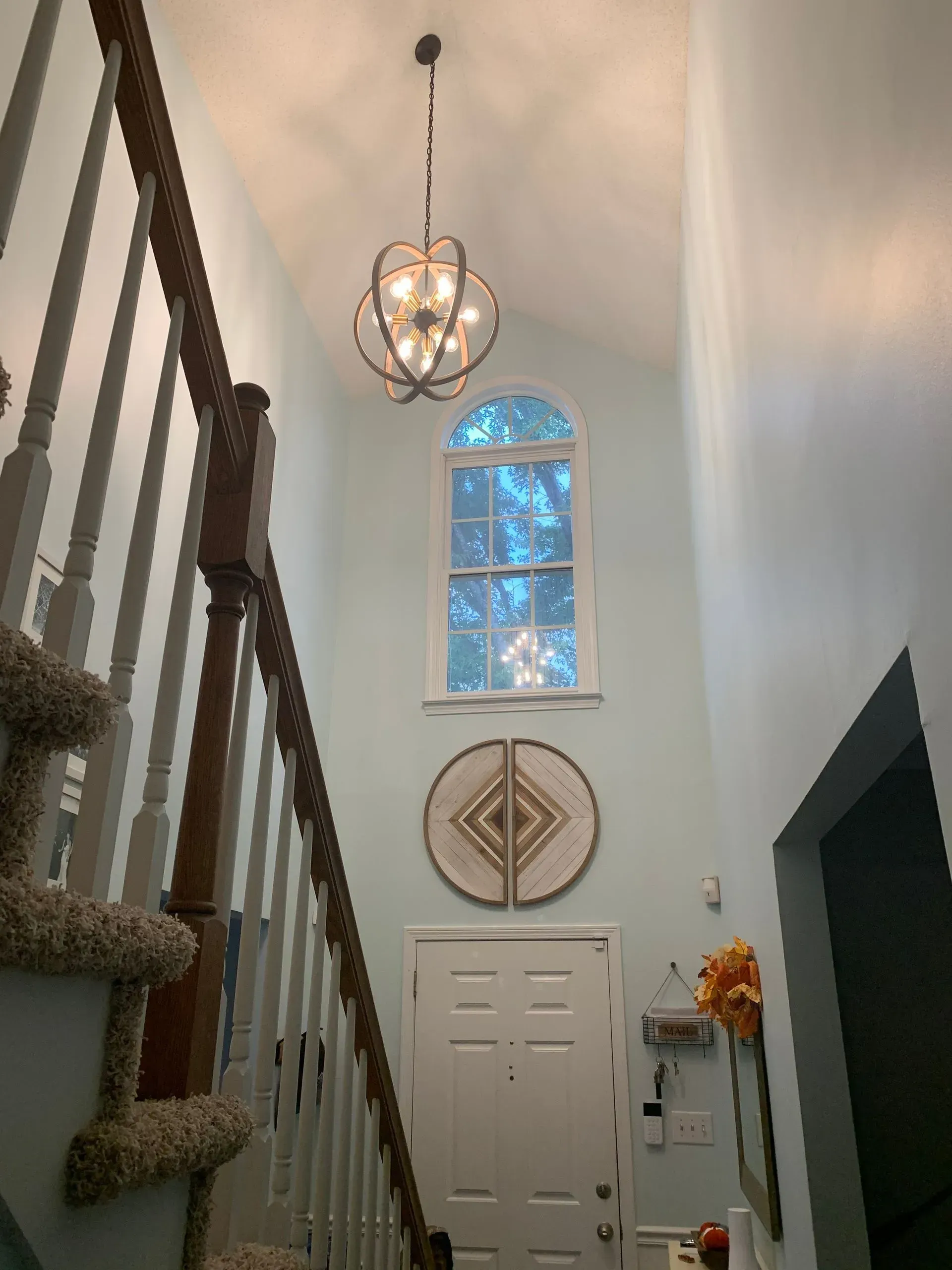 Entryway with staircase, high ceiling, round chandelier, arched window, and door. Turquoise walls.