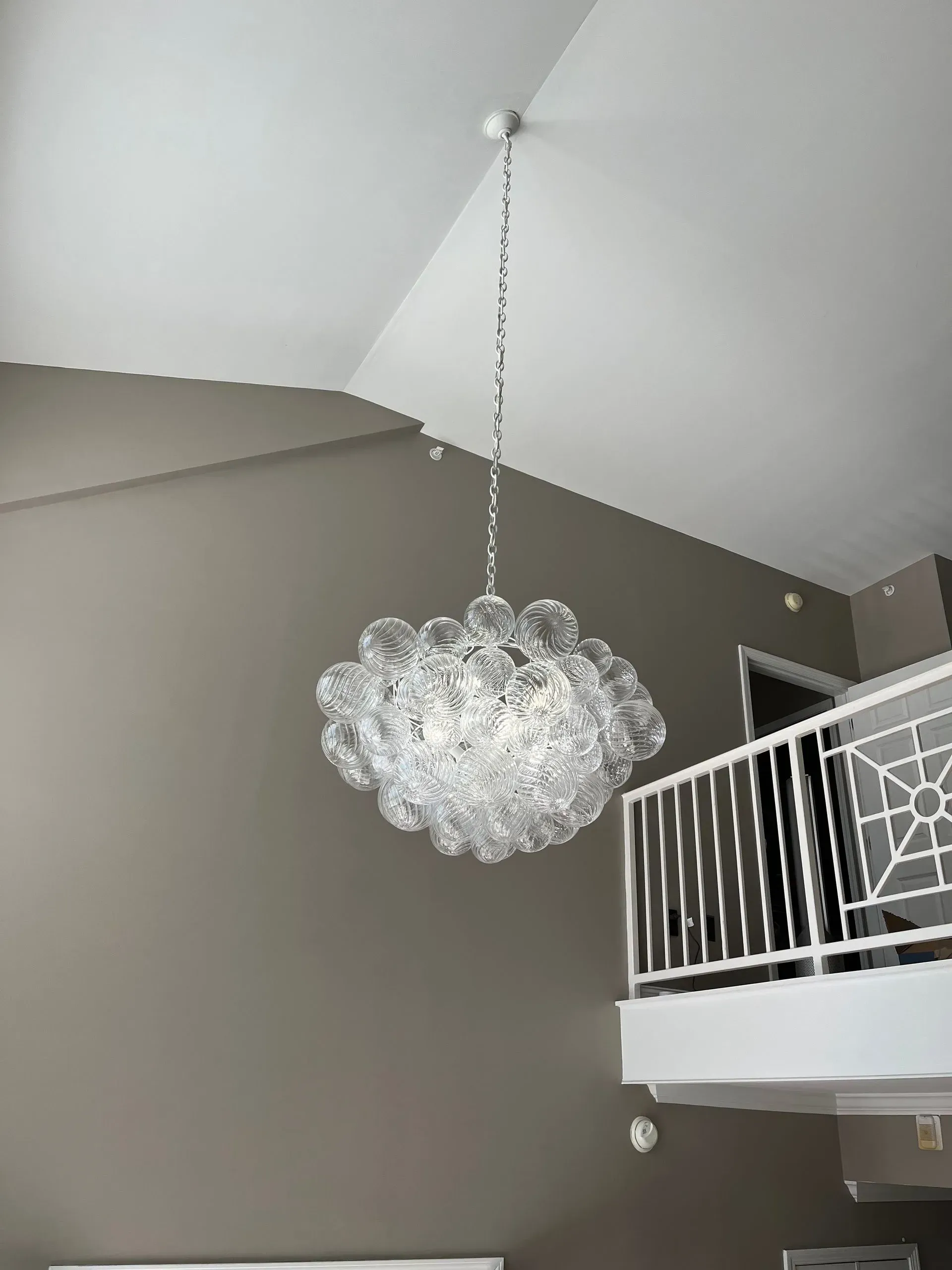 Crystal chandelier hanging from a tall, angled white ceiling in a room with a loft.