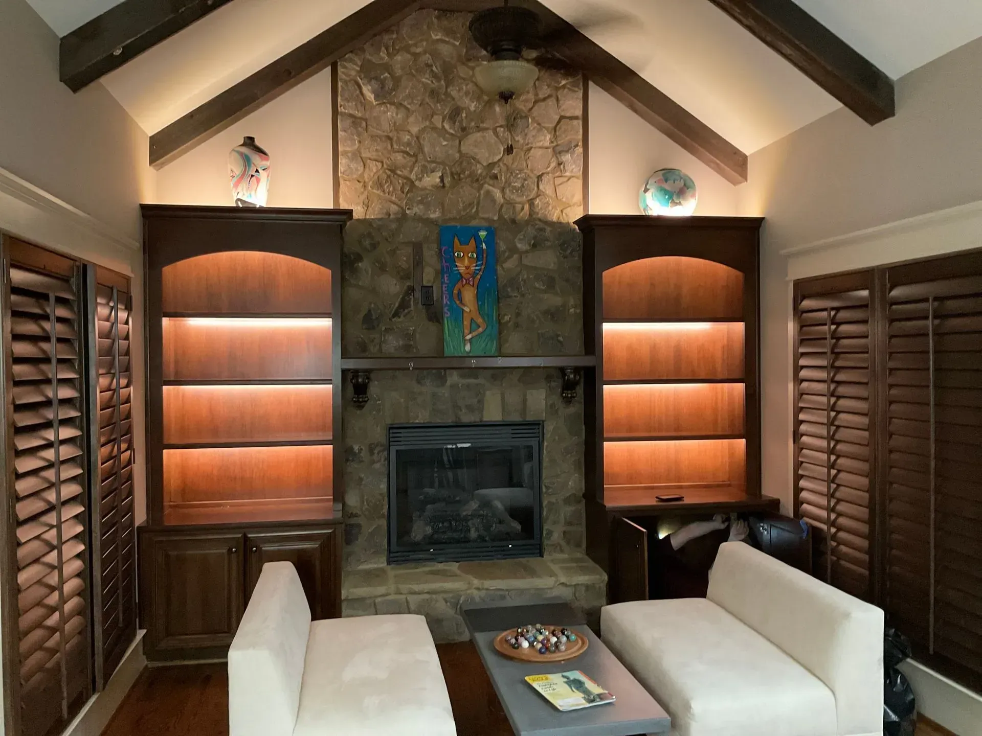 Cozy living room with stone fireplace, built-in bookshelves with lighting, and white couches.