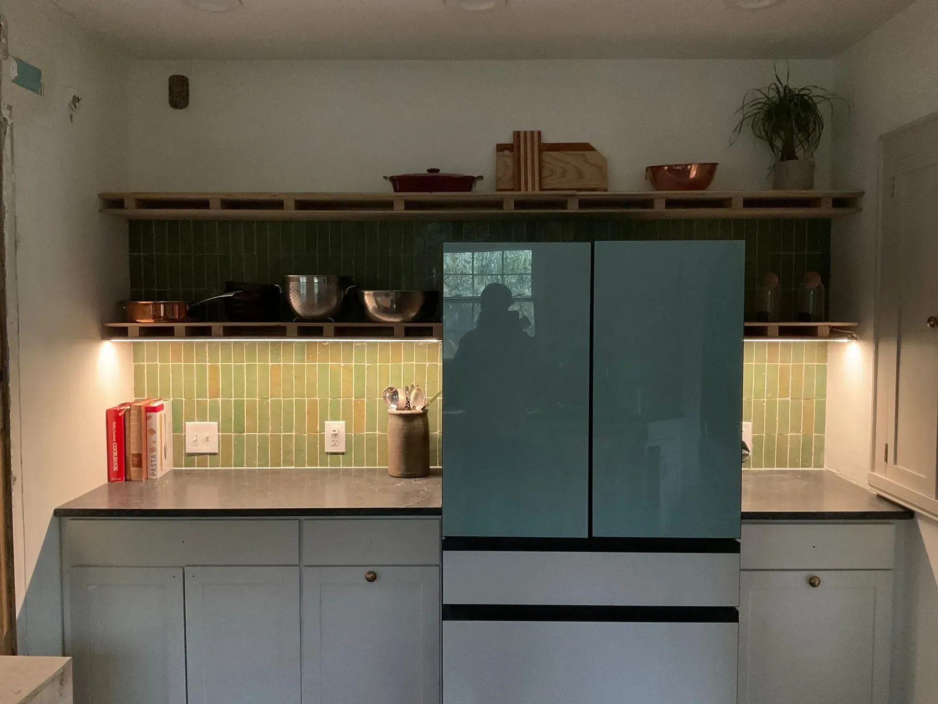 Kitchen with green tile backsplash, open shelves holding bowls, and a teal refrigerator.