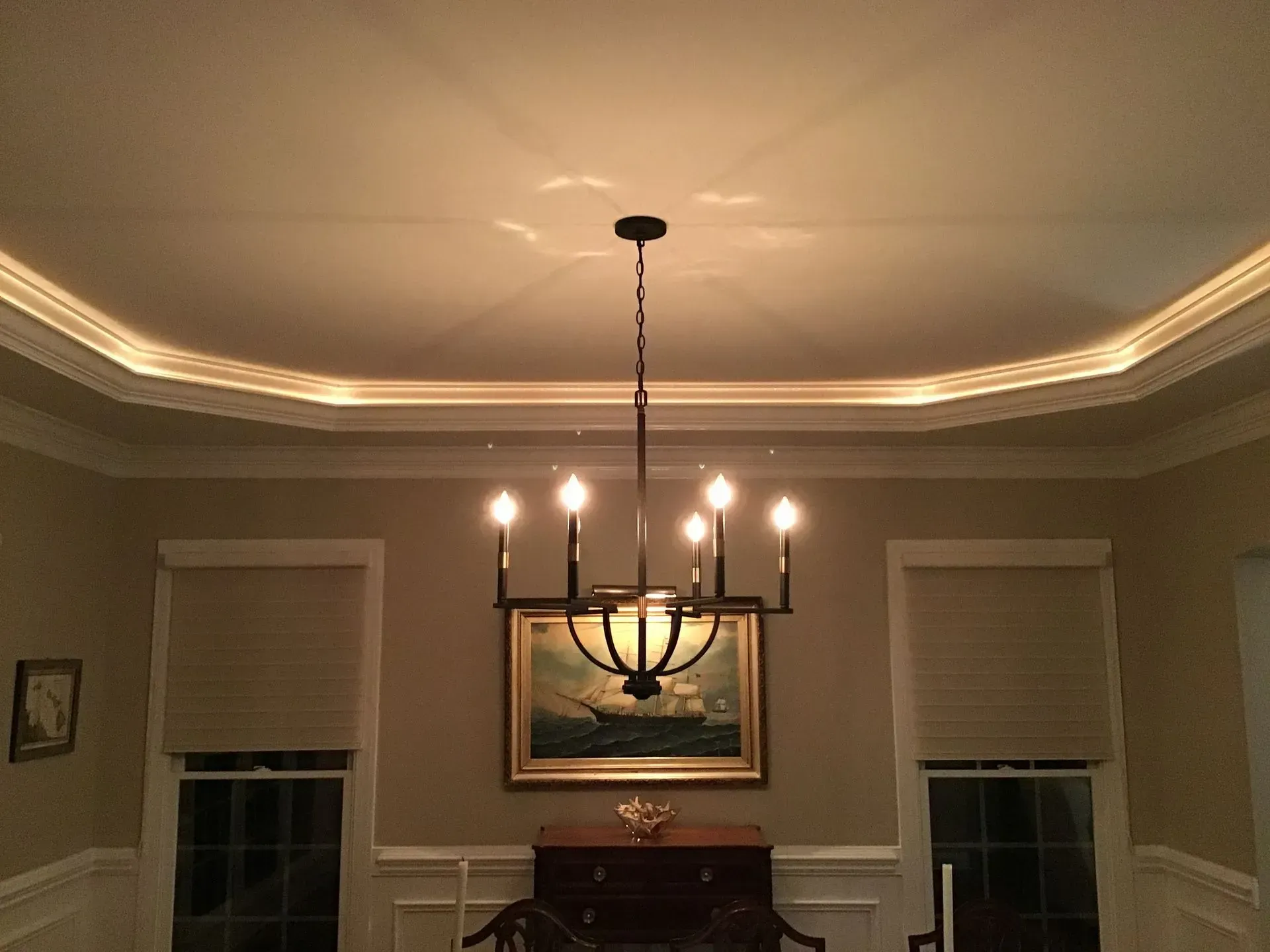 Dining room with a chandelier, crown molding with recessed lighting, and a ship painting.