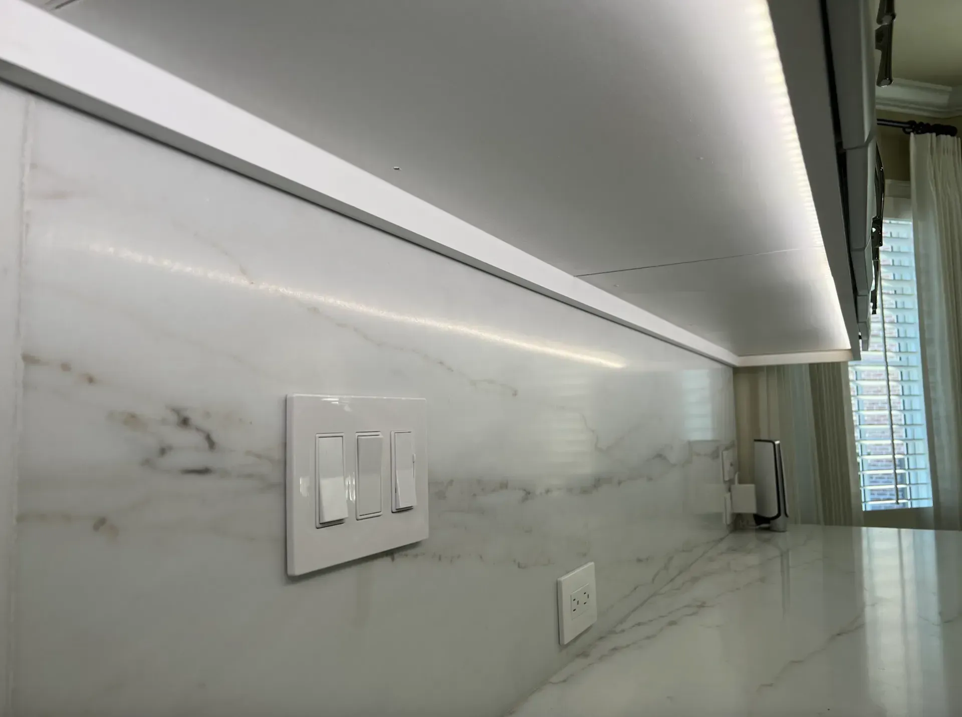 White marble backsplash with under-cabinet lighting and light switch.