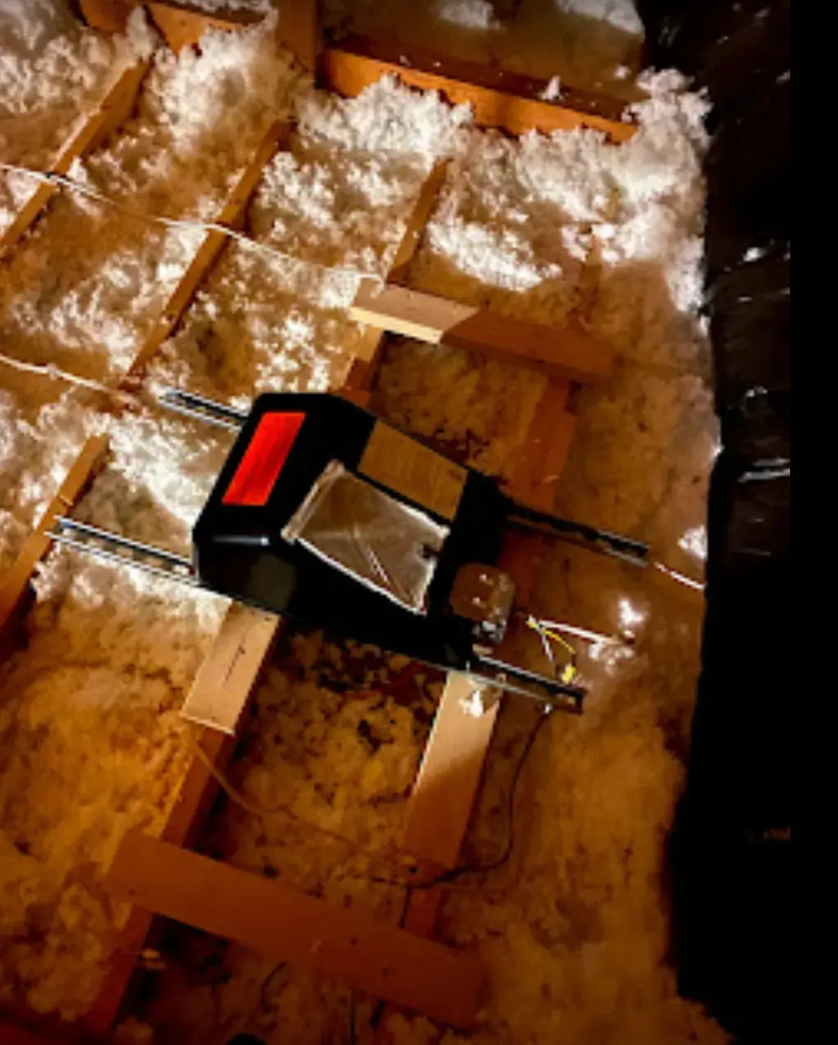 Garage door opener in an attic, with wooden beams and insulation.