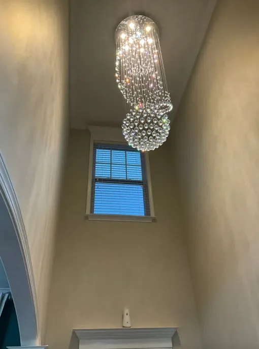 Crystal chandelier hangs in a tall room with a window and white walls.