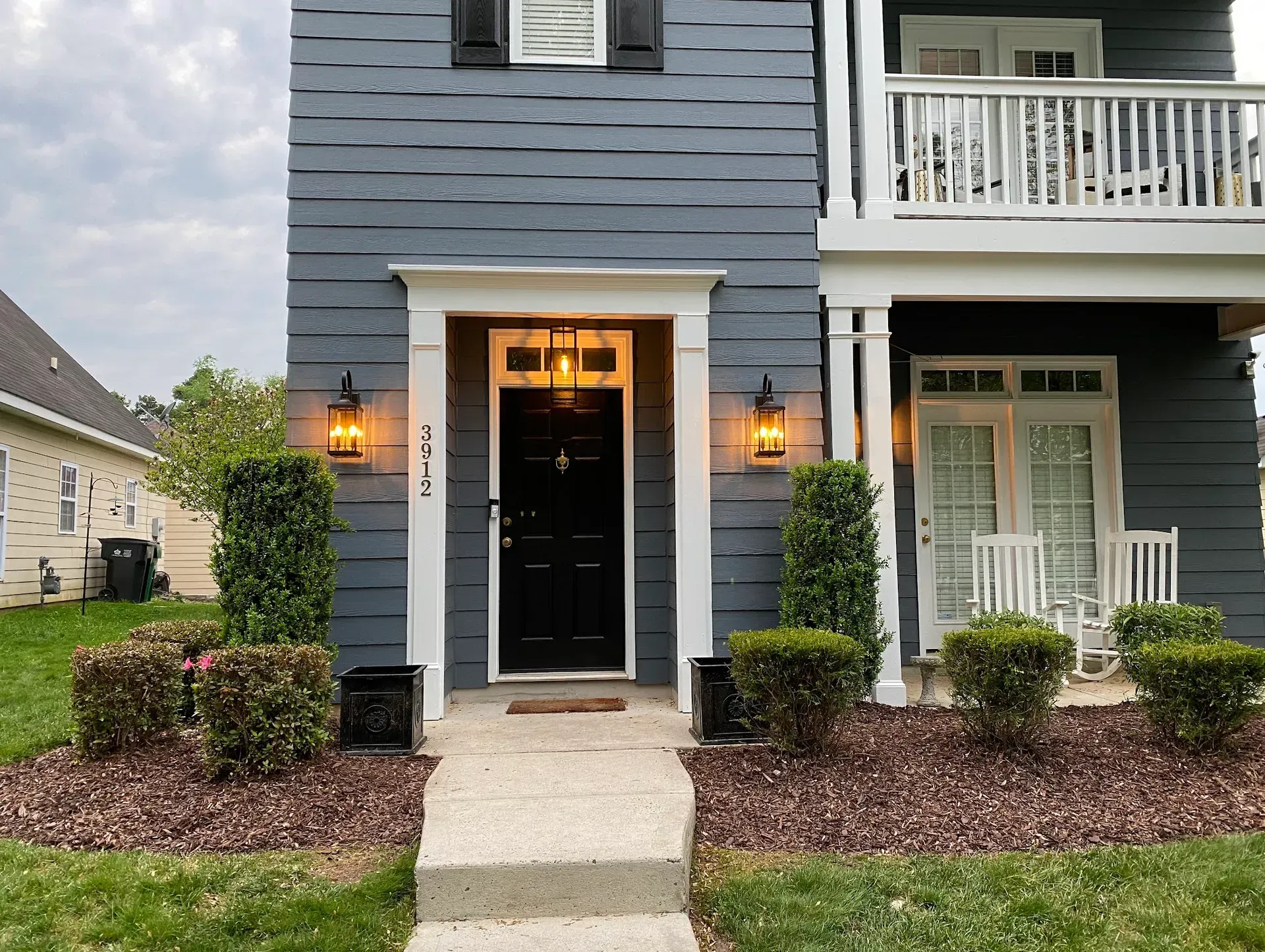 Dark gray townhouse exterior with a black door, two sconces, and porch with white railing.