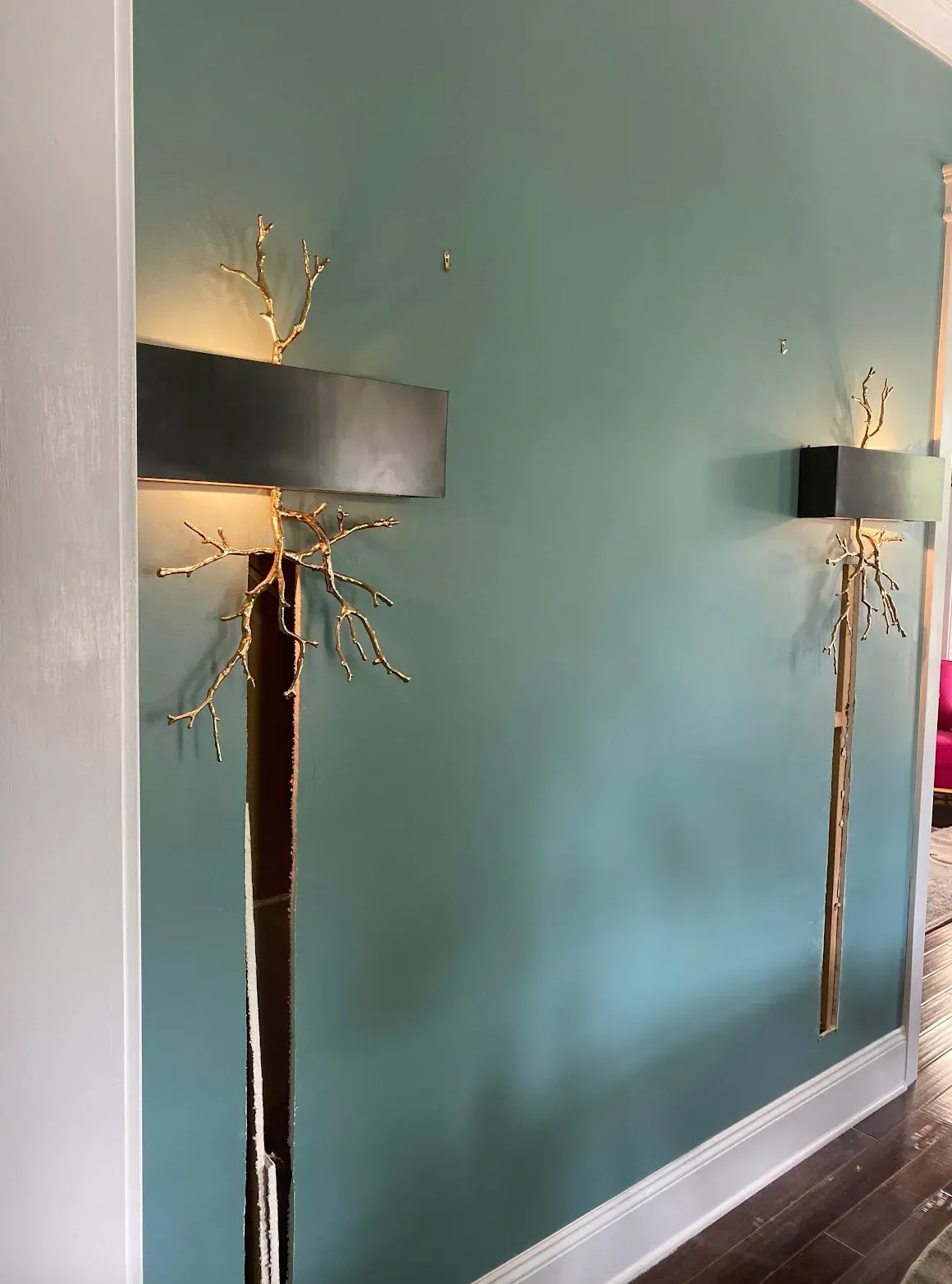 Two wall sconces with gold branch designs on a teal wall, near a white doorway.