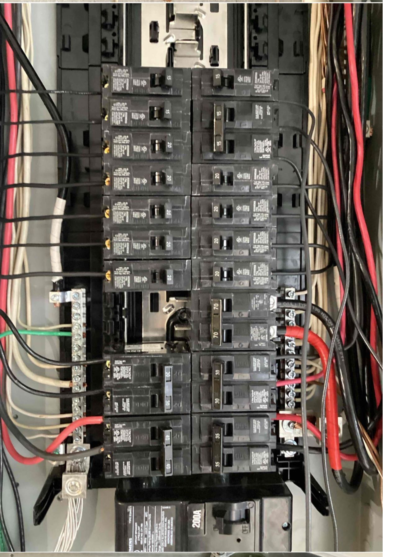 Electrical circuit breaker panel with numerous breakers, wires, and labels.