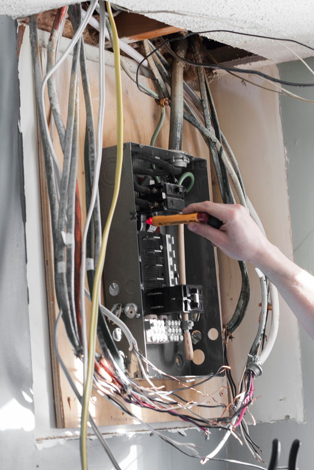 Open electrical panel with wires; hand using a voltage tester.