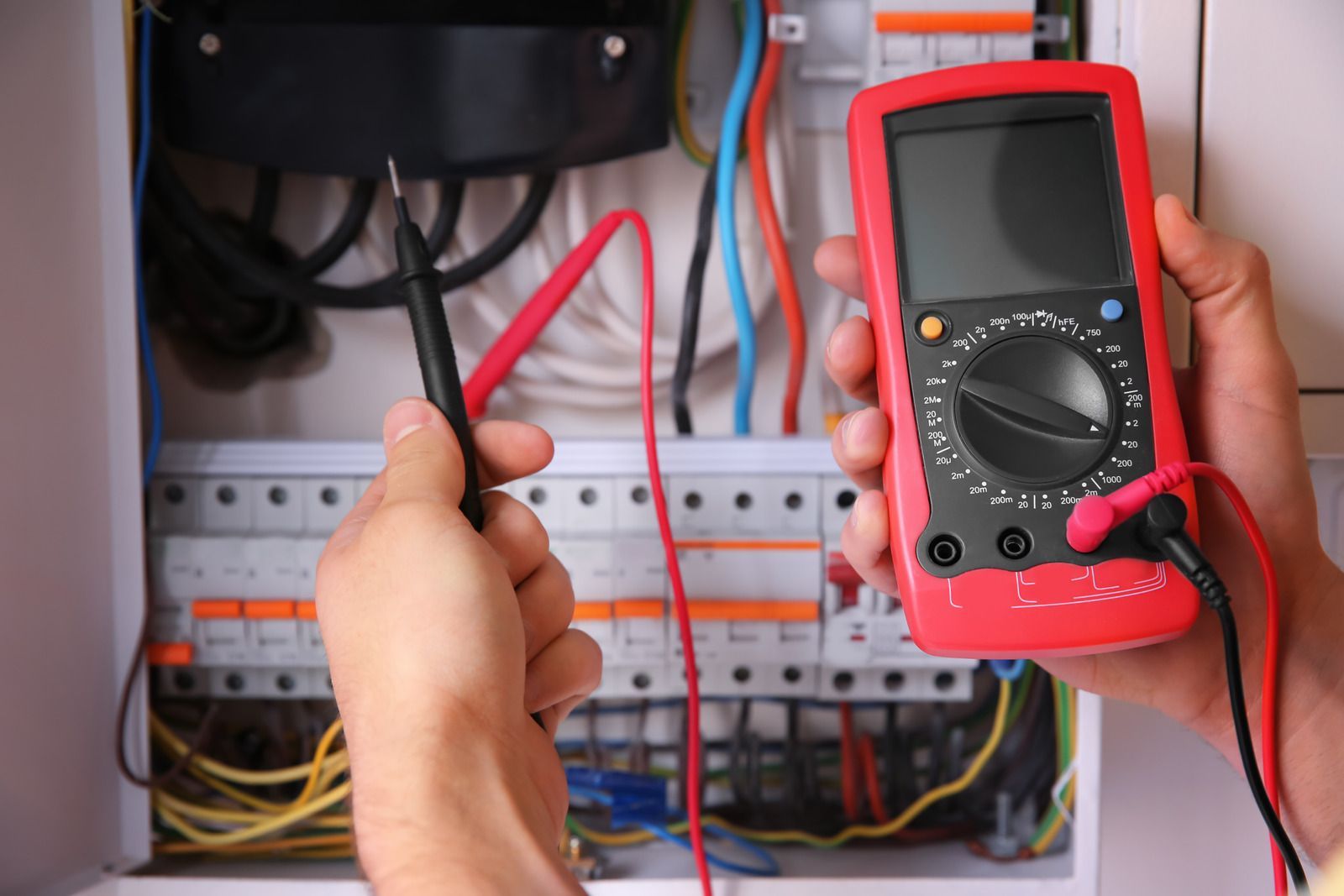 Person using a red multimeter to test electrical wiring in a panel.