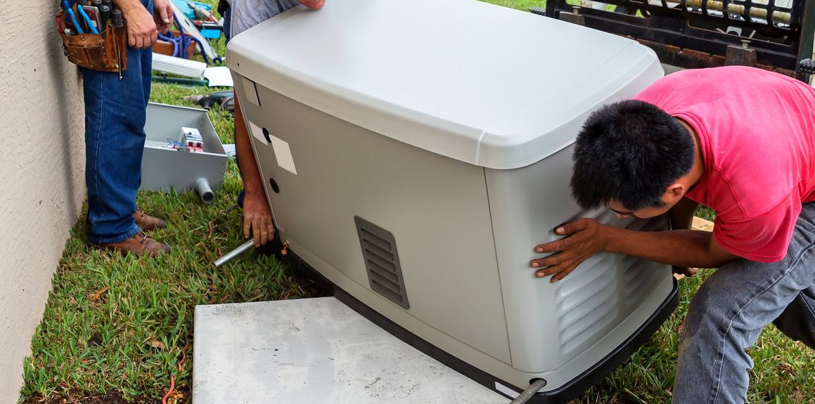 Two men installing a generator on a concrete pad next to a house. One man is wearing a pink shirt.