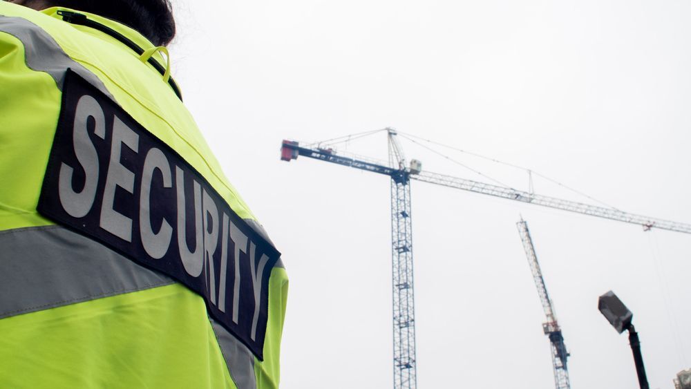 A Security Guard Stands In Front Of A Construction Crane — Hire A Security Guard in Blackwater, QLD