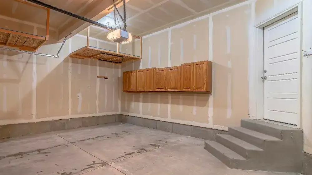 Empty basement with unfinished walls, concrete floor, wooden cabinets, stairs, and ceiling ductwork.