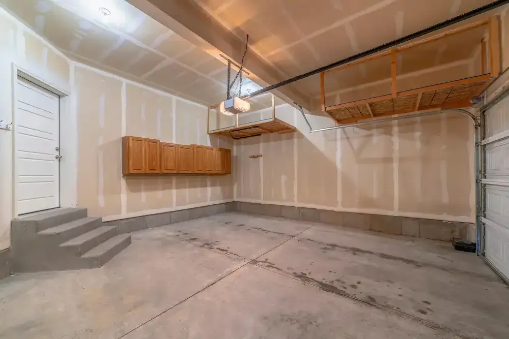 Empty garage with concrete floor, storage cabinets, and overhead shelves. Interior view.