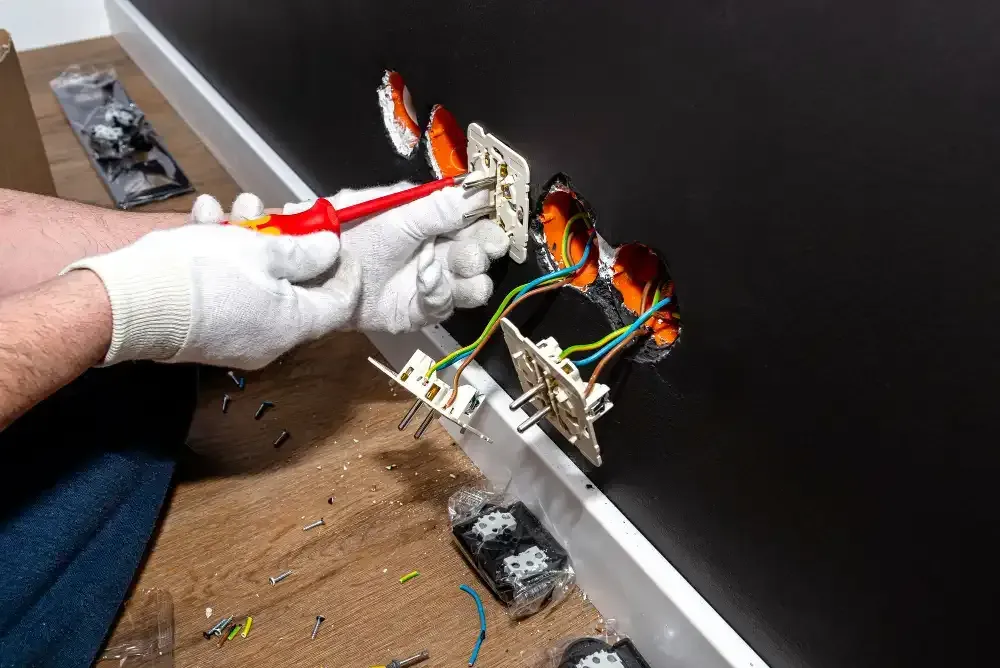 Person in gloves installing electrical outlets on a black wall, using pliers.