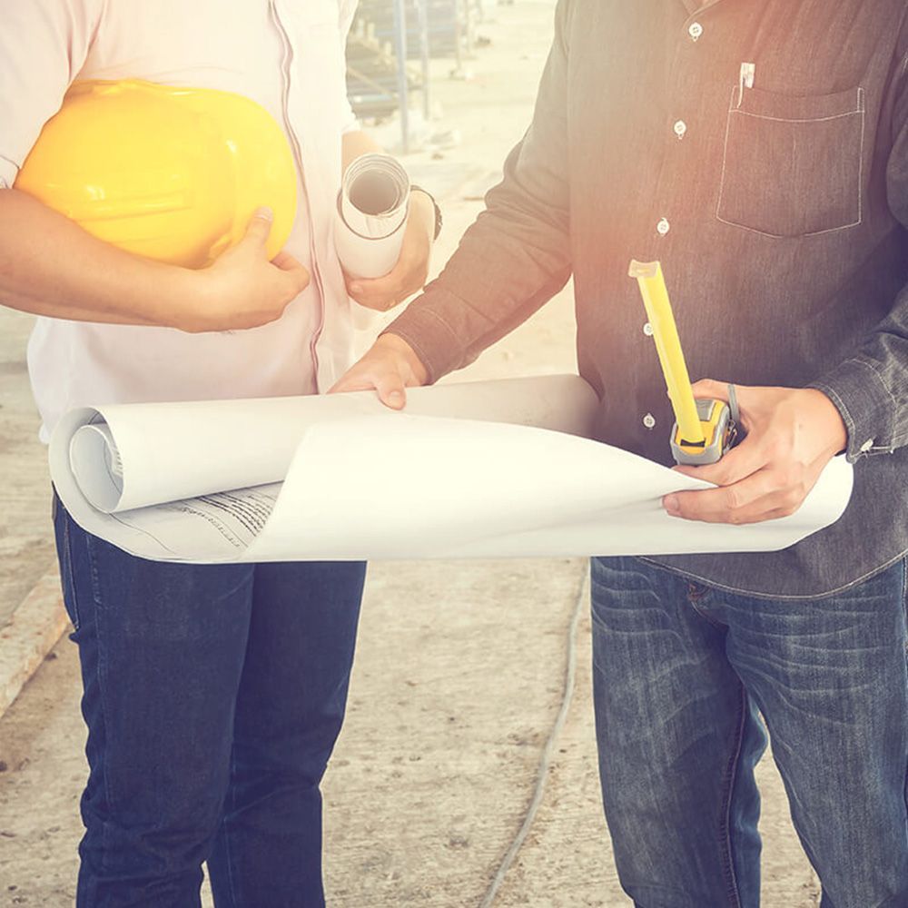 A man and a woman are standing next to each other holding blueprints and a tape measure.