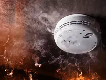 A smoke detector is surrounded by smoke and flames in a room.