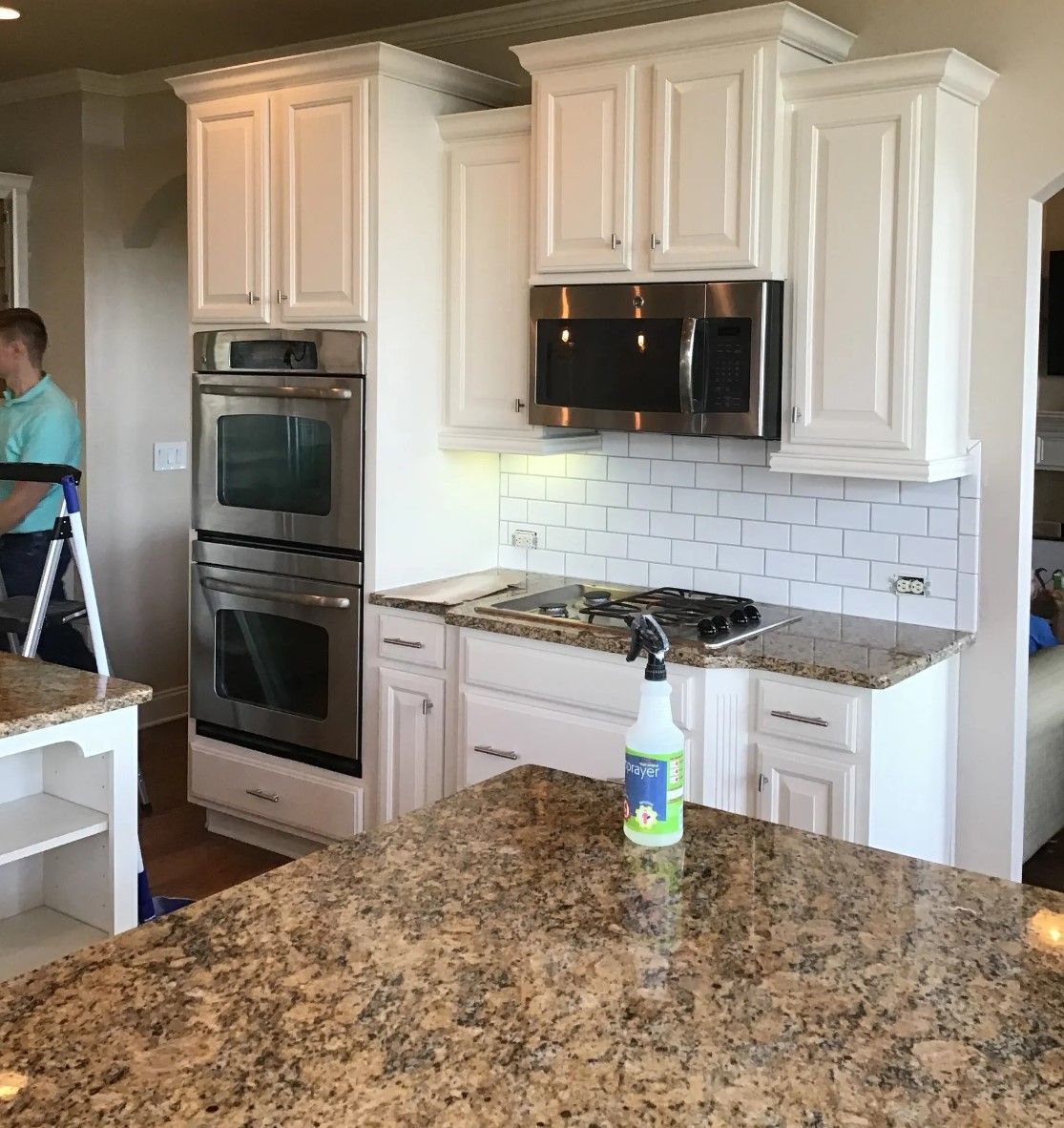 White kitchen cabinets with appliances and granite countertops. A person is visible.