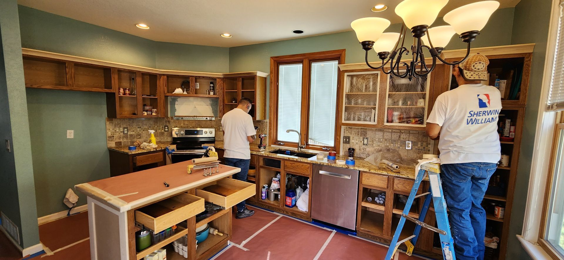 Two people renovating a kitchen with exposed cabinets, an island, and a chandelier.
