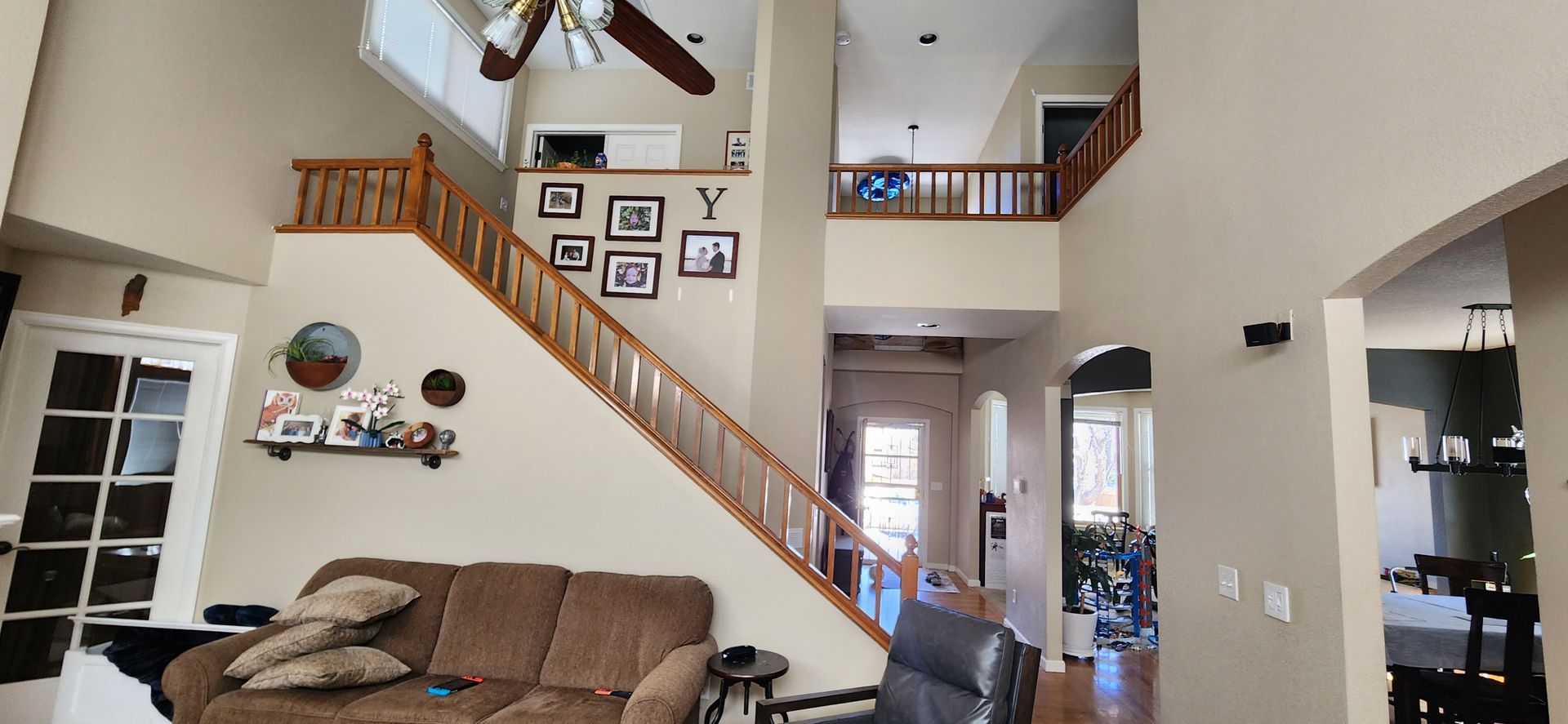 Interior of a home with a staircase, a balcony, a couch, and a ceiling fan.