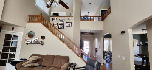 Interior of a home with a staircase, a balcony, a couch, and a ceiling fan.
