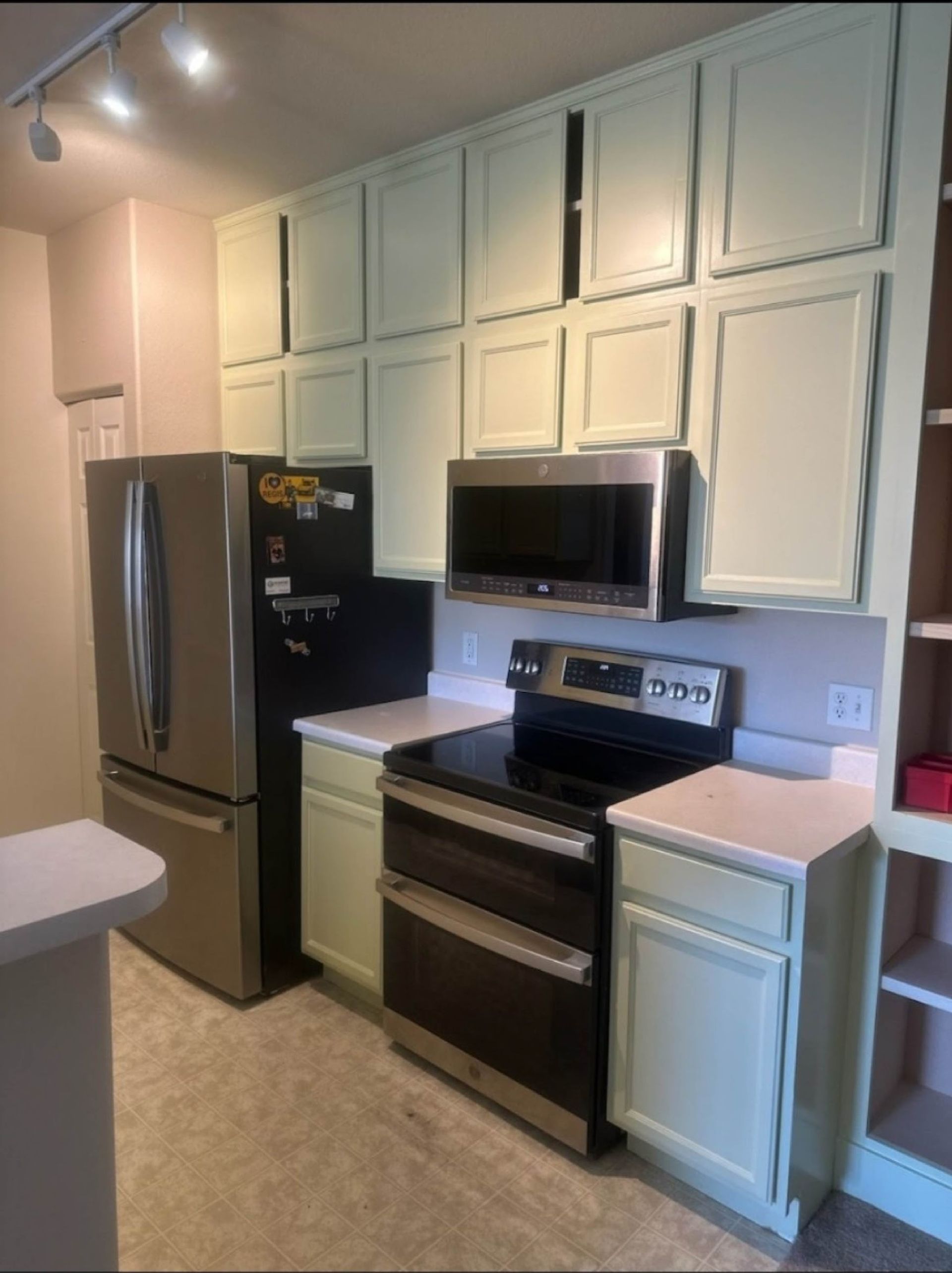 Kitchen with light green cabinets, stainless steel appliances, and a white countertop.