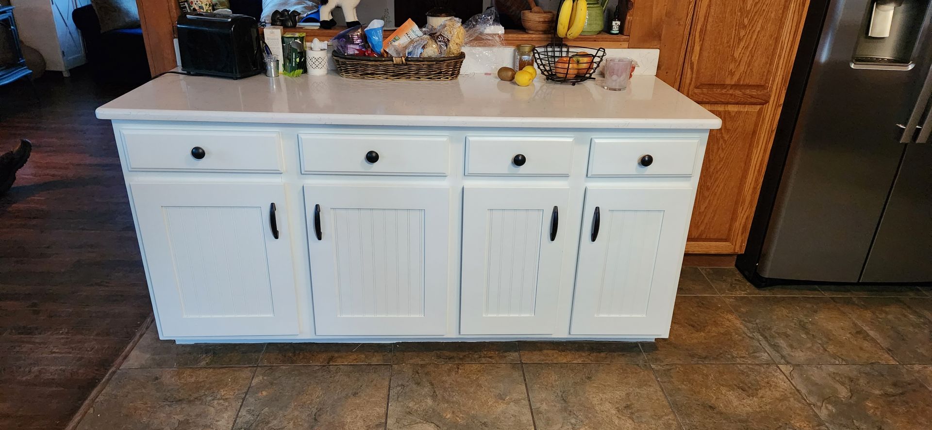 White kitchen island with countertop, cabinets, and black hardware in a kitchen setting.