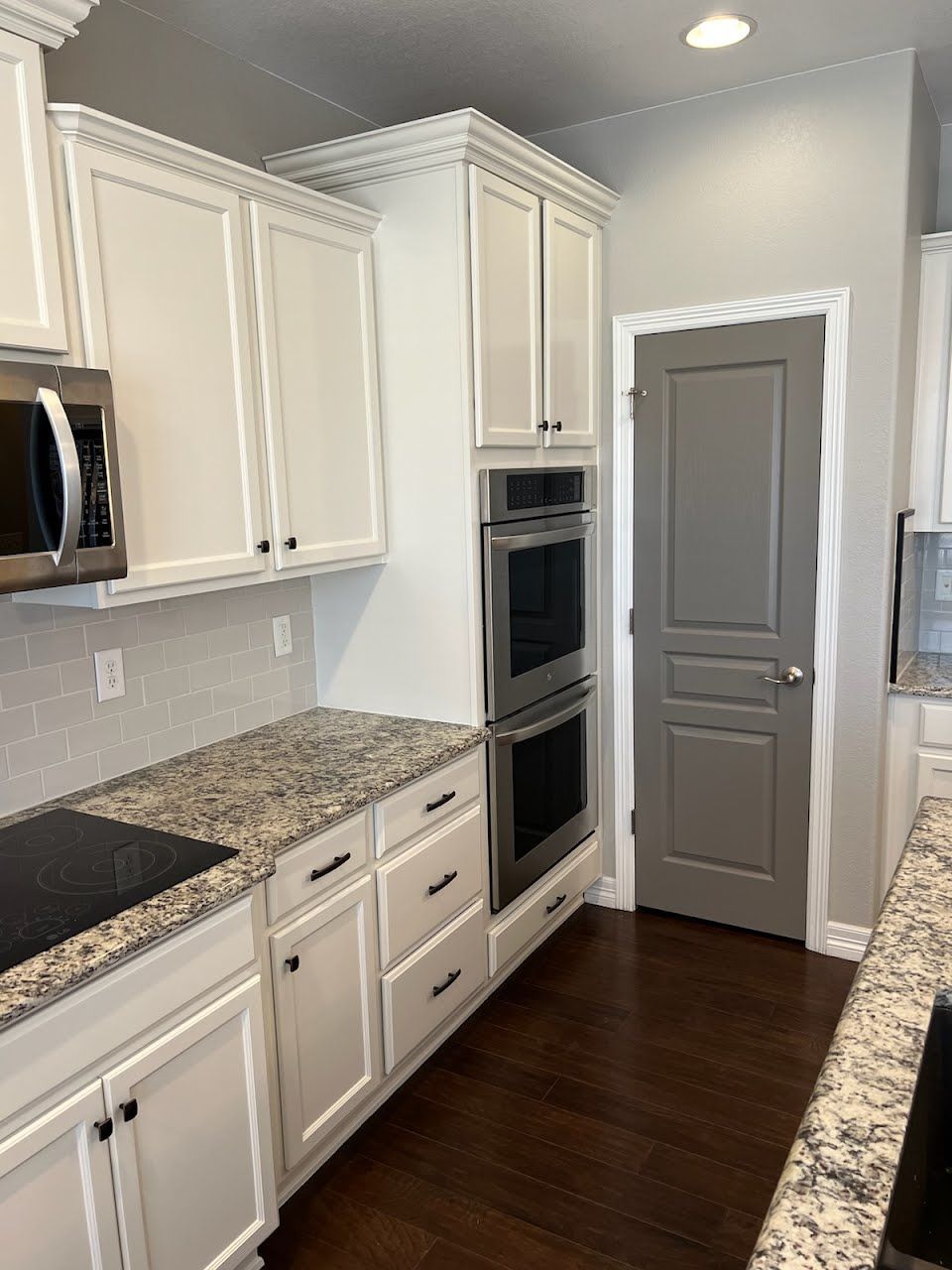 White kitchen with granite countertops, stainless steel appliances, and a gray pantry door.