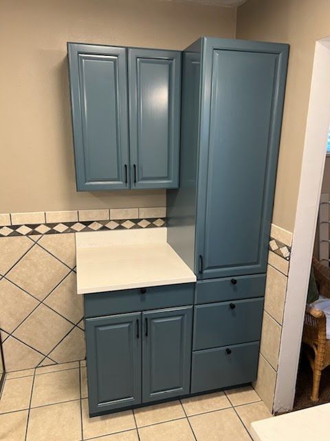 Blue kitchen cabinets with white countertop and tile backsplash.